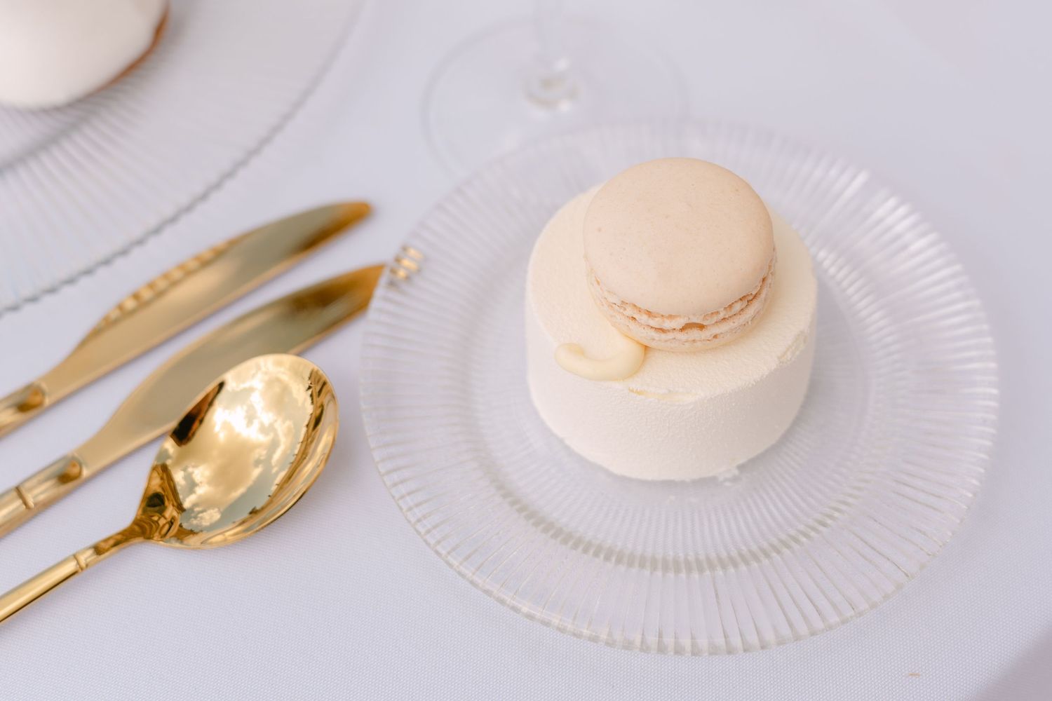 Elegant white macaron served on a glass plate with gold utensils on a white tablecloth. Villa Mosconi Bertani