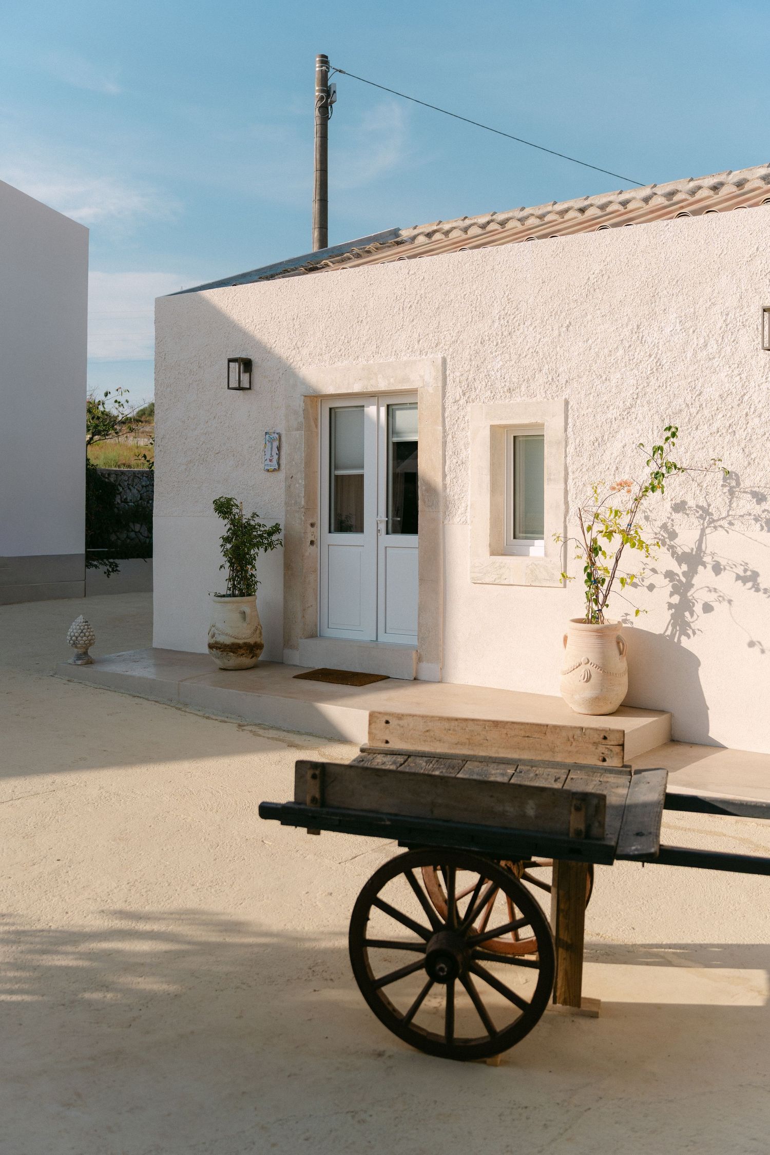 Whitewashed Mediterranean building entrance with vintage wooden cart and potted plants.