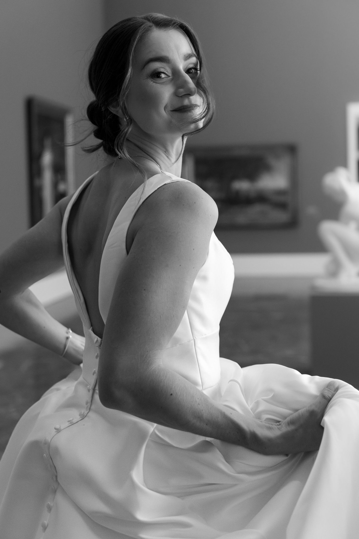 Black and white portrait of a bride in a sleeveless white wedding gown looking over her shoulder with a gentle smile.