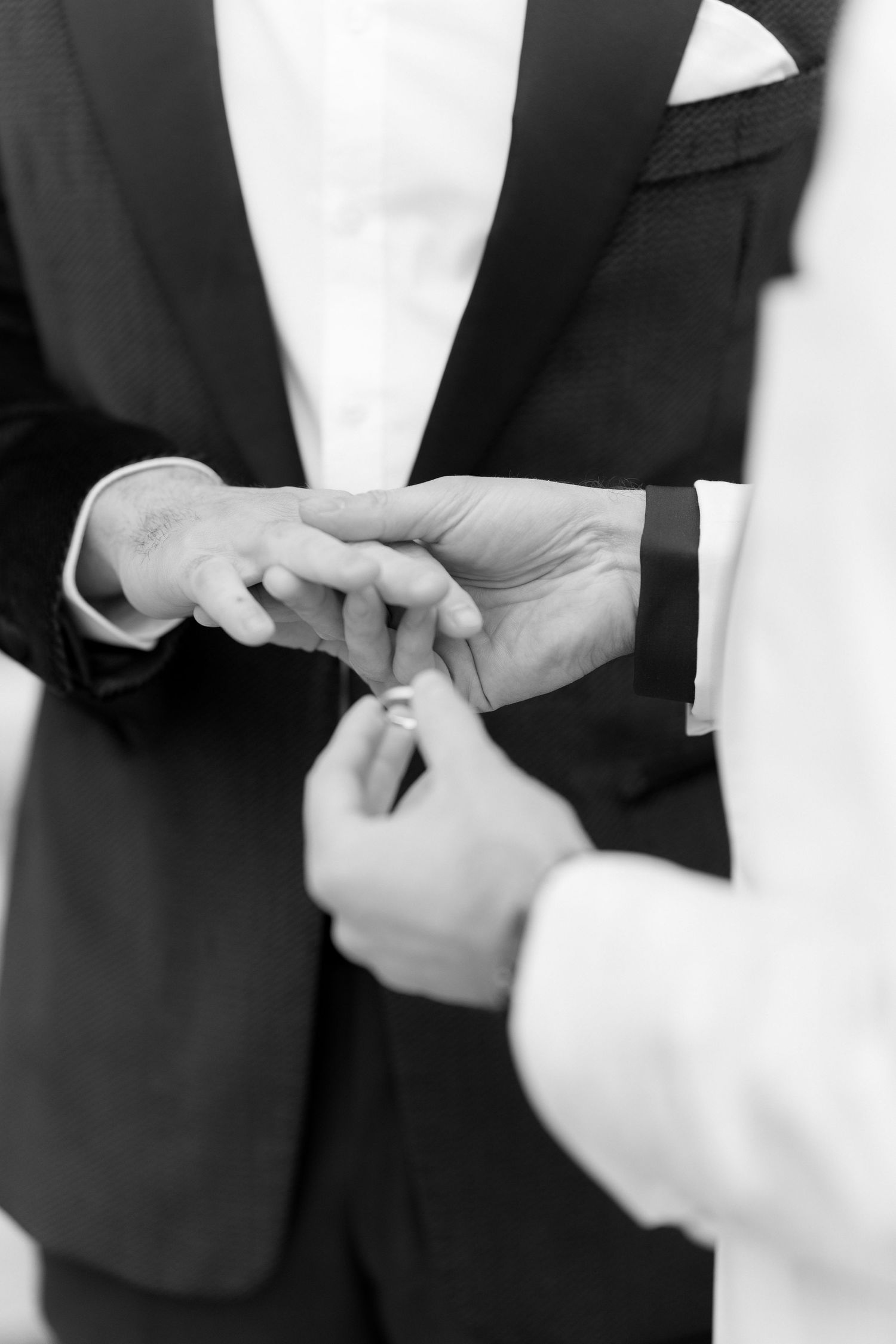Black and white close-up of hands exchanging wedding rings during a ceremony.