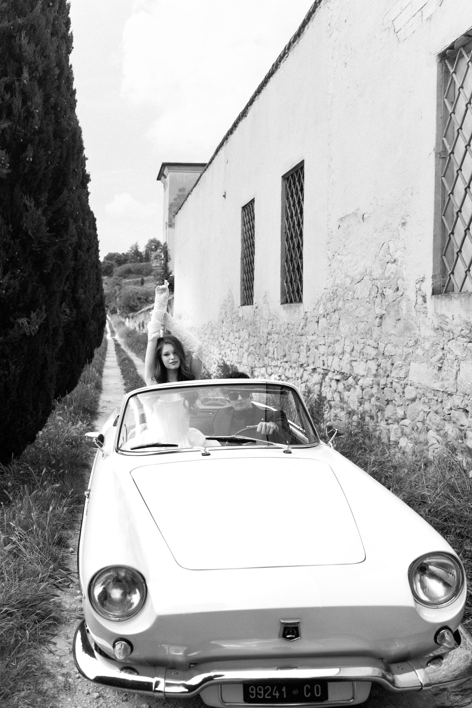 A vintage white Renault Caravelle convertible car parked against a rustic white building wall in black and white.