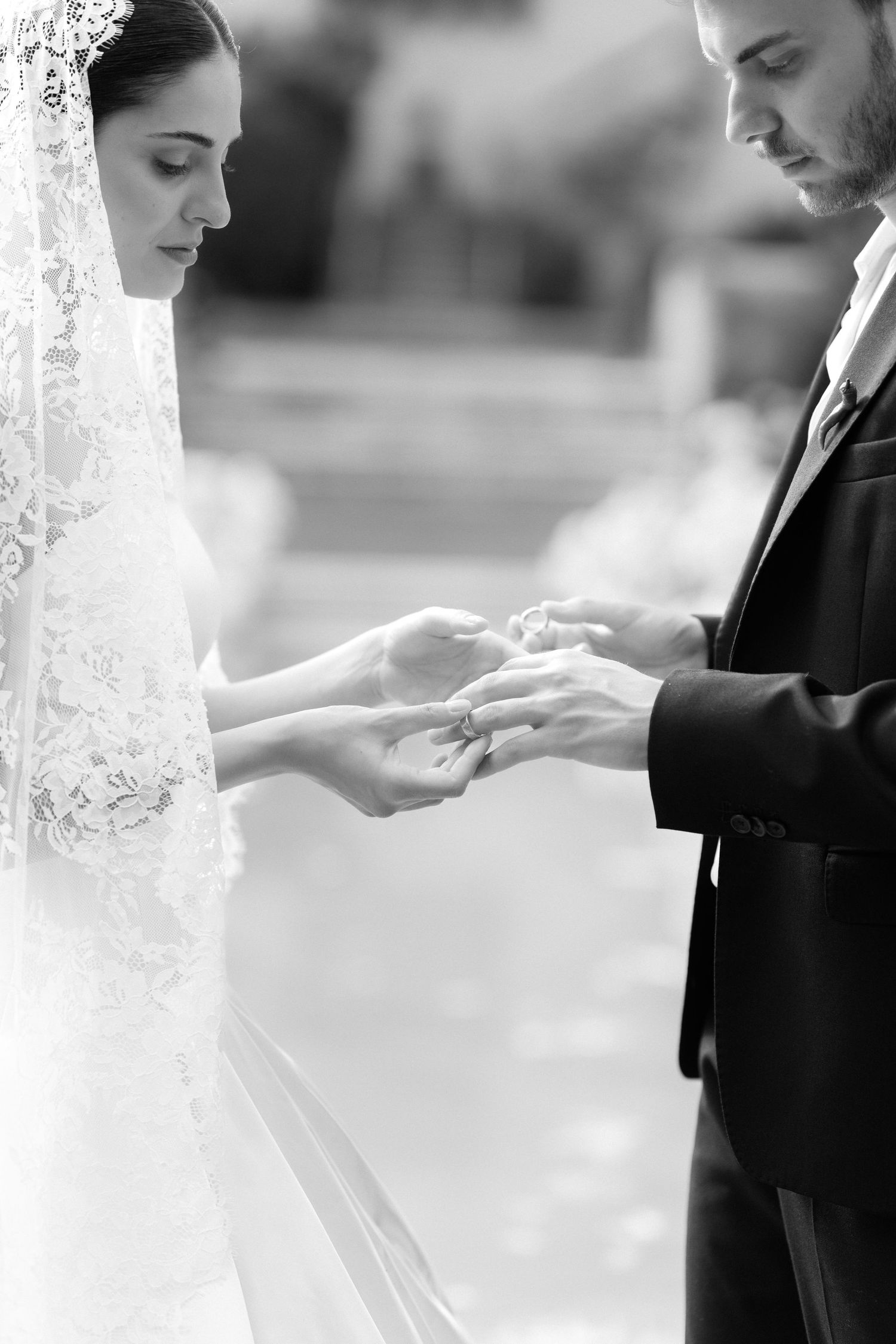 Black and white photo of groom placing wedding ring on bride's finger during ceremony.