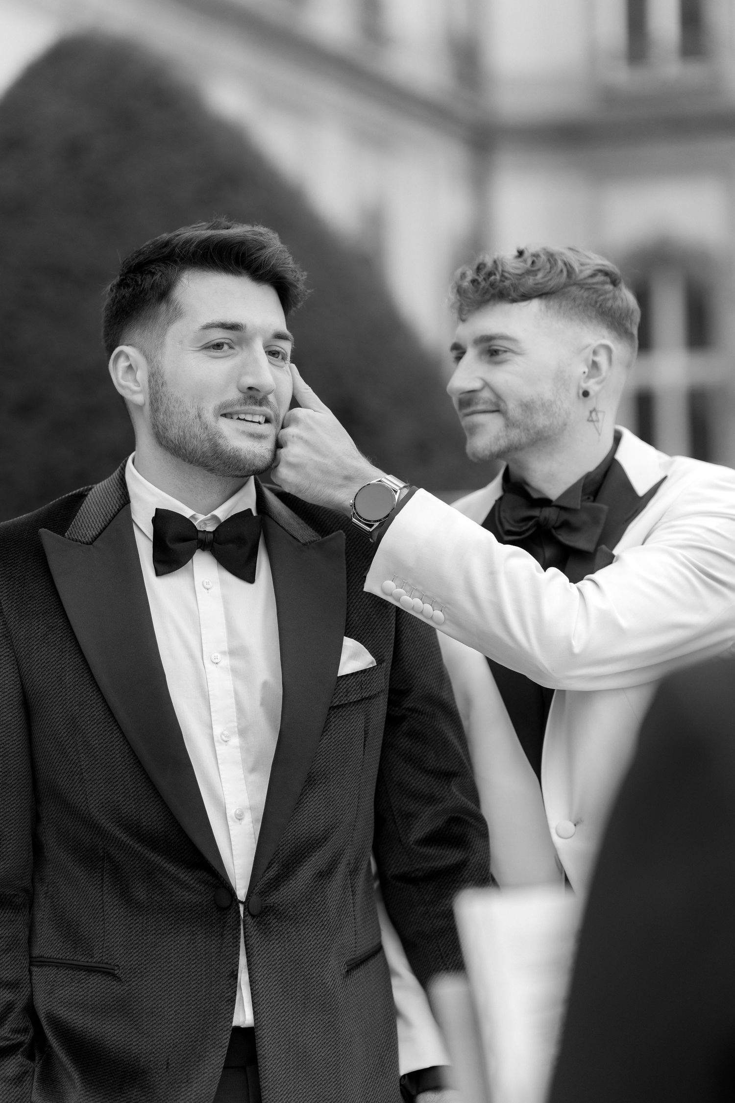 Black and white portrait of a tender moment between two grooms dressed in tuxedos at their wedding.