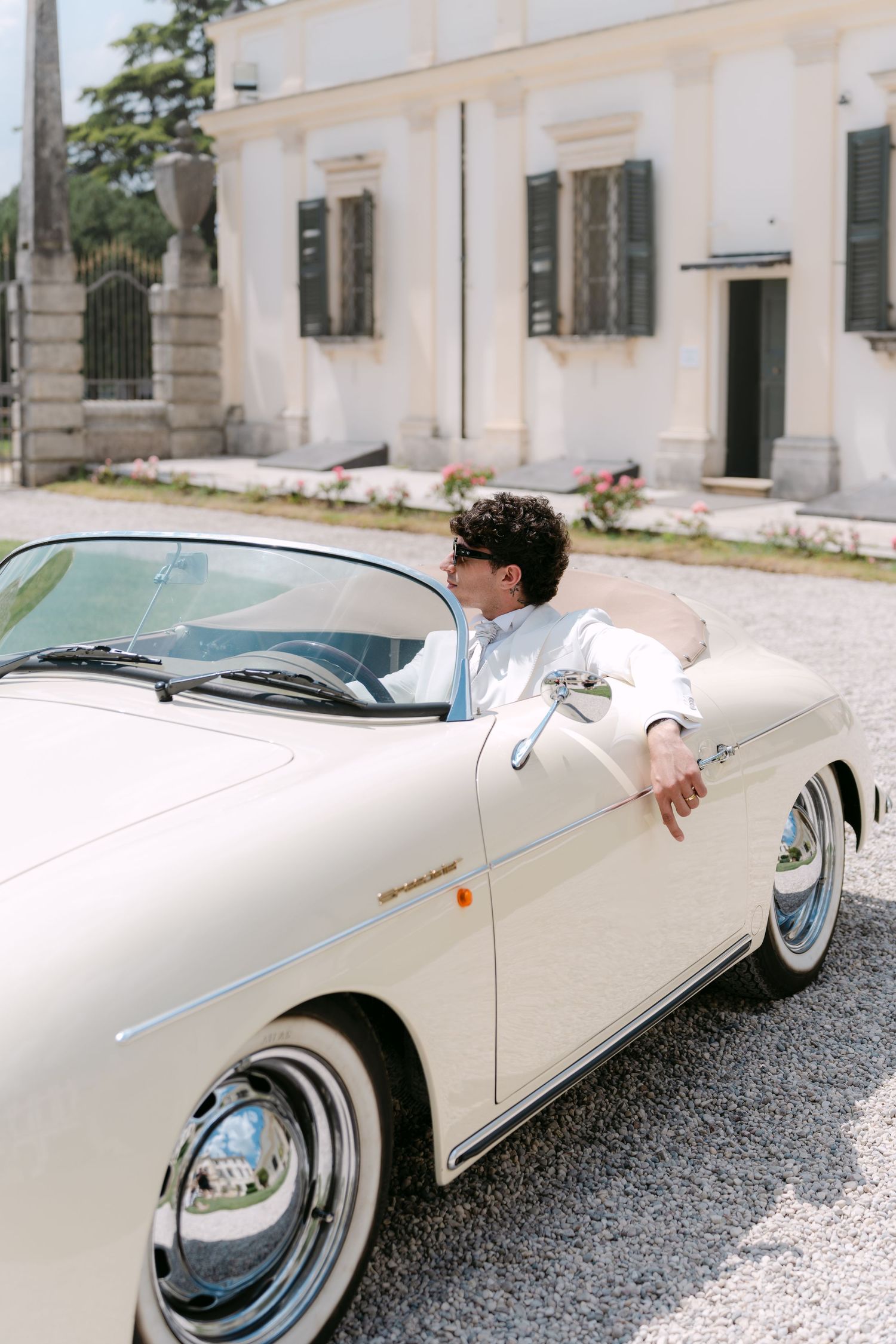 A classic white Porsche 356 Speedster parked in front of a vintage villa on a gravel driveway. Villa Mosconi Bertani