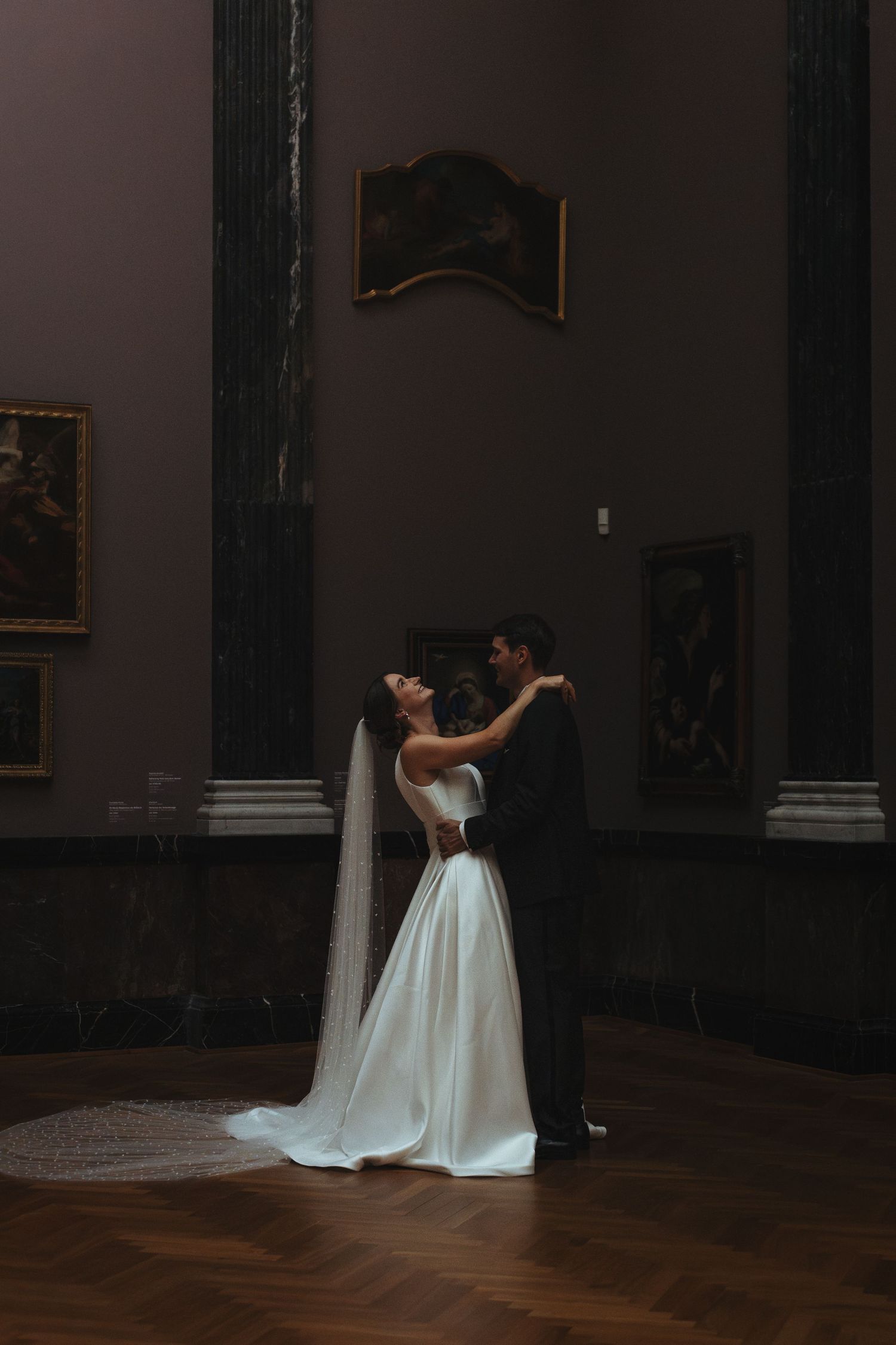 A couple shares an intimate dance in a dimly lit ballroom with ornate walls and hardwood floors.