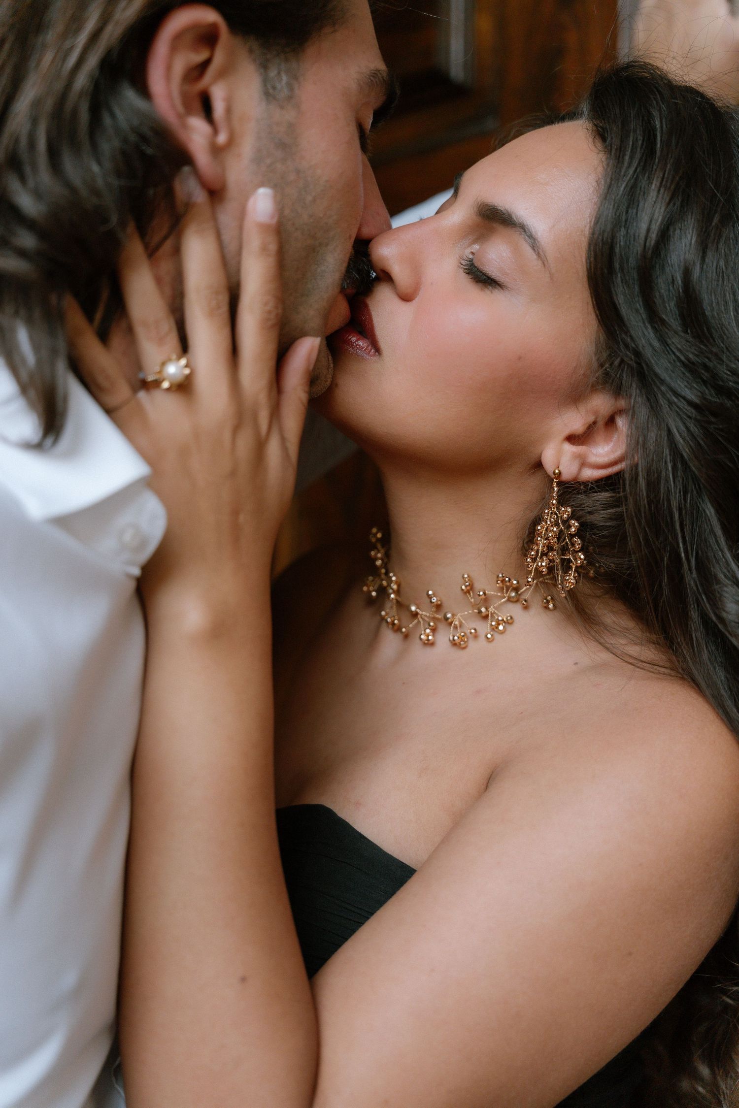 Couple sharing a romantic kiss, woman wearing gold floral earrings and strapless black top.