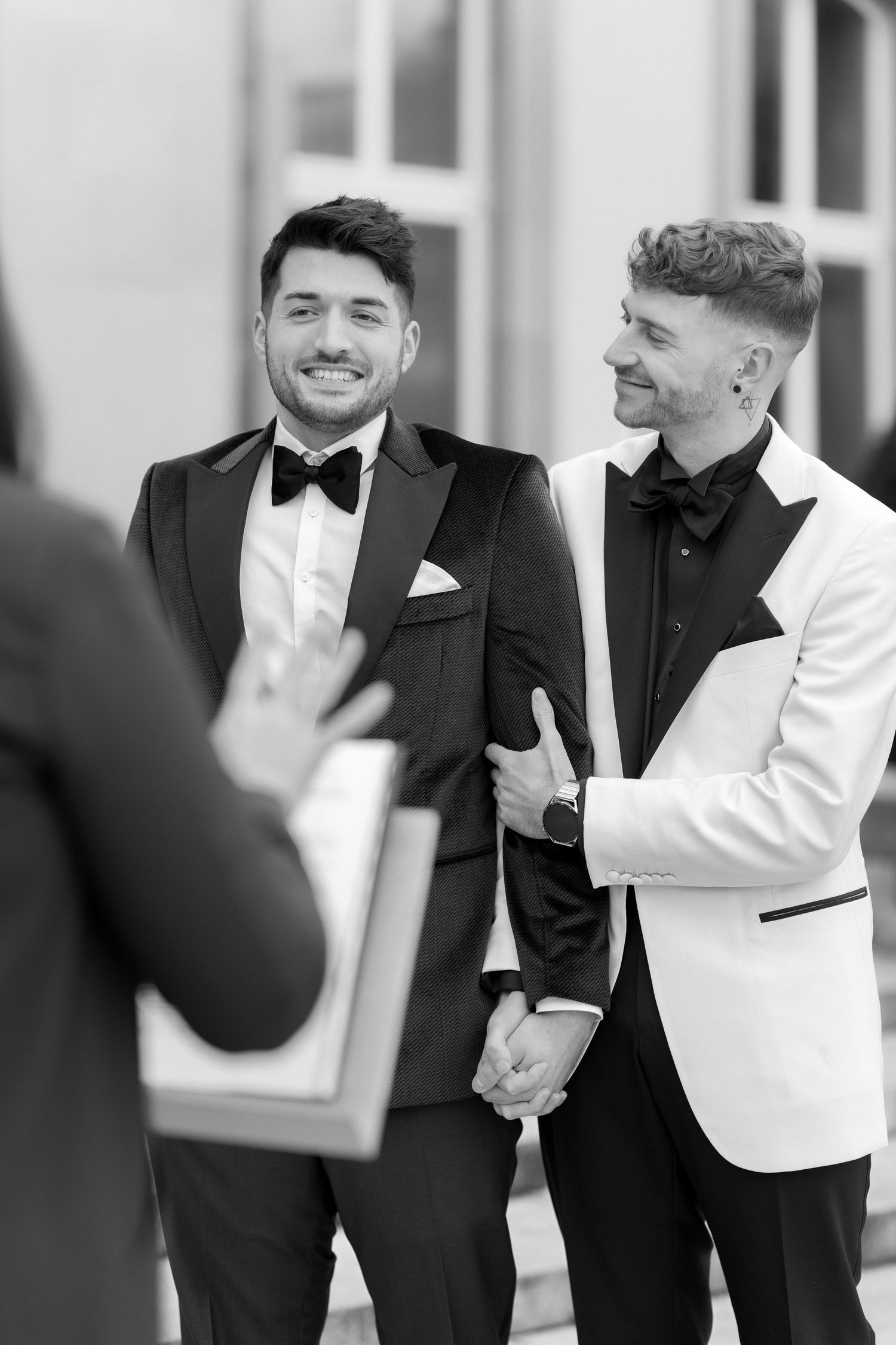 Two people share a candid moment at a formal event, wearing black and white tuxedos with bow ties.