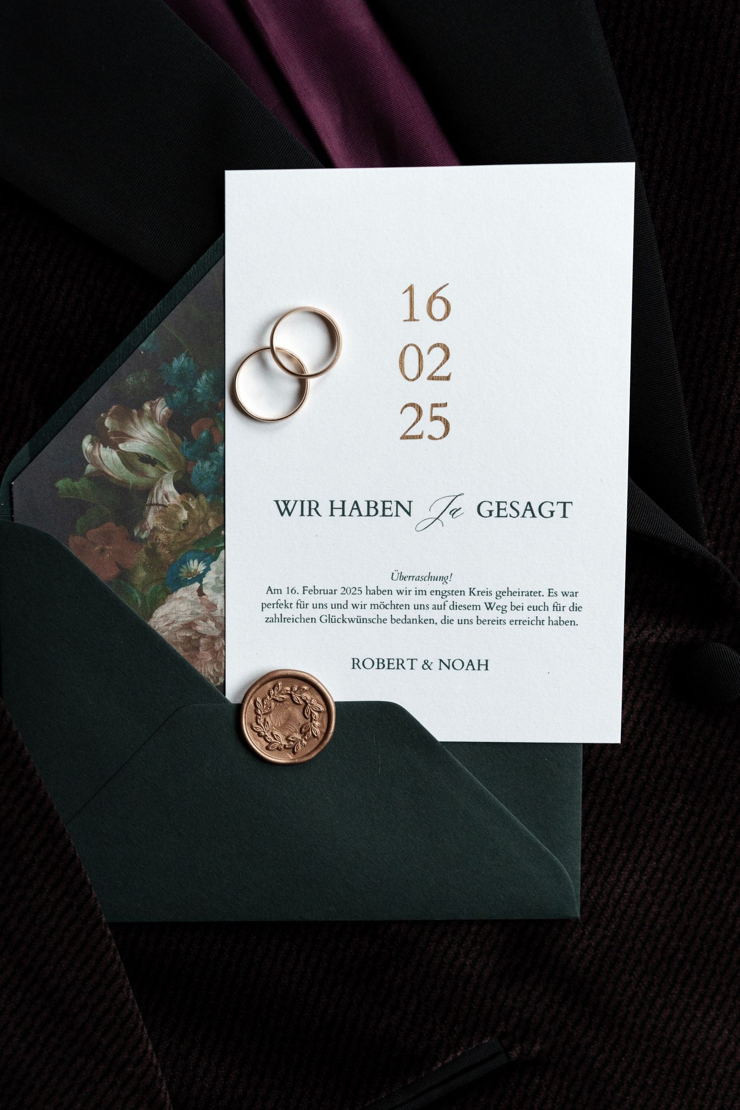 Elegant wedding invitation with gold date text, two rings, and a wax seal on dark green envelope.