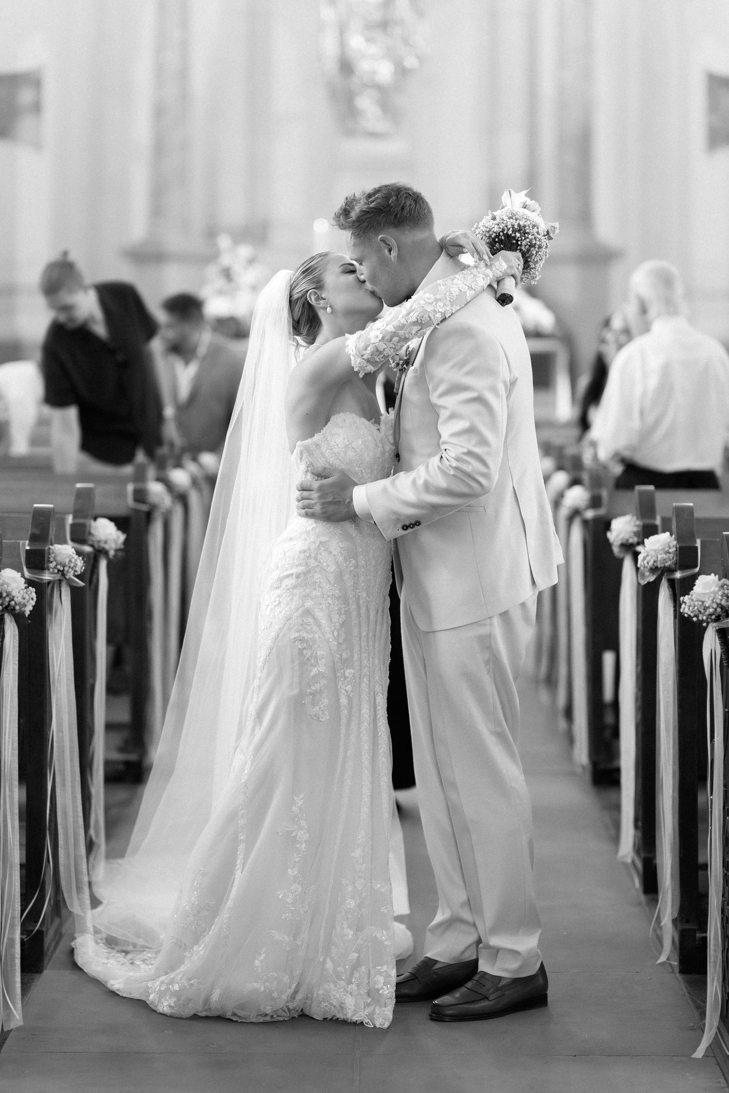 Black and white wedding photograph showing three couples sharing romantic kisses in a church aisle.