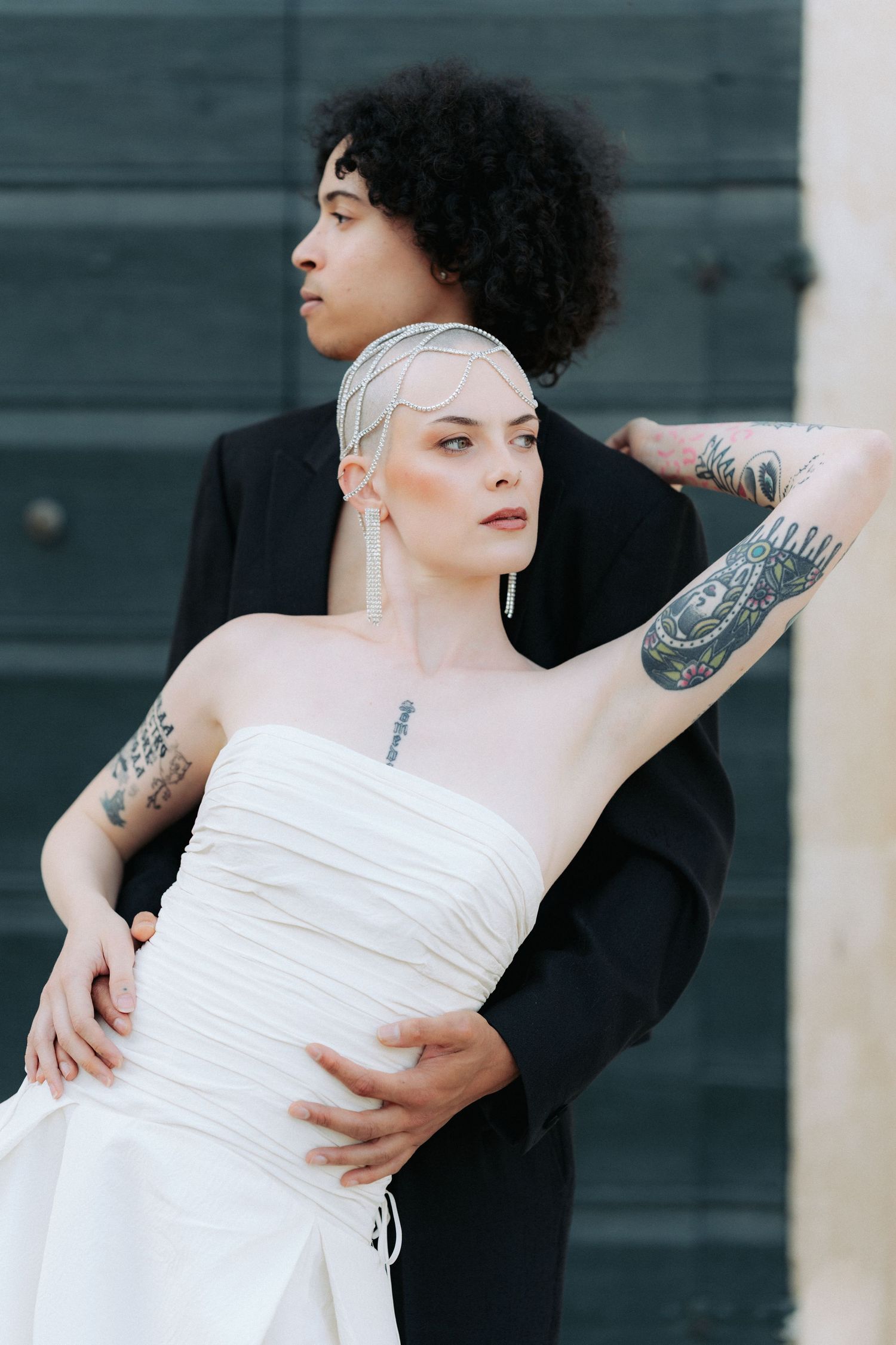 A romantic wedding photo series showing a couple embracing against a dark wall, with the person in white wearing a strapless dress.