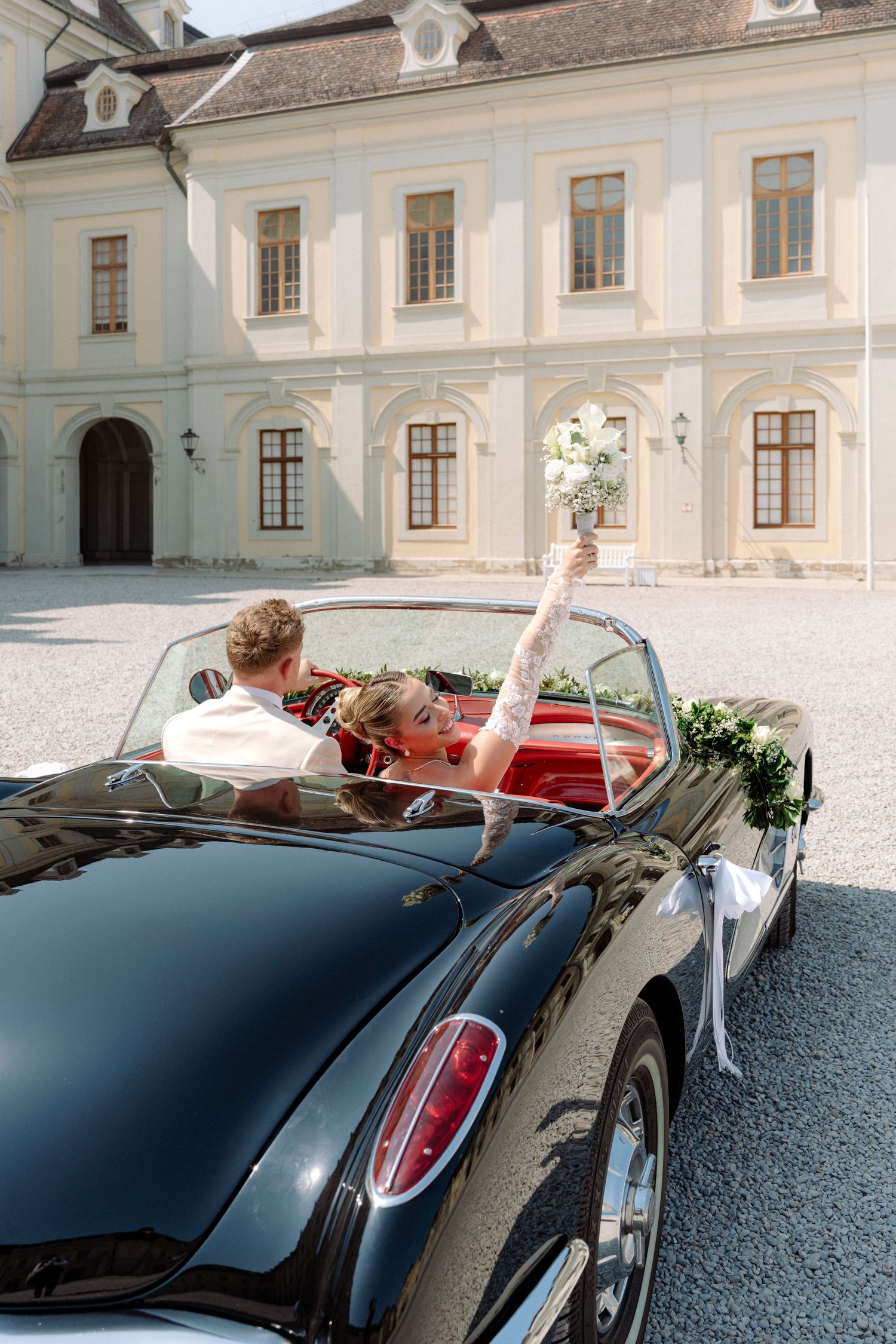 Vintage black convertible sports car parked in front of an elegant white European palace or mansion. Schloss Ludwigsburg