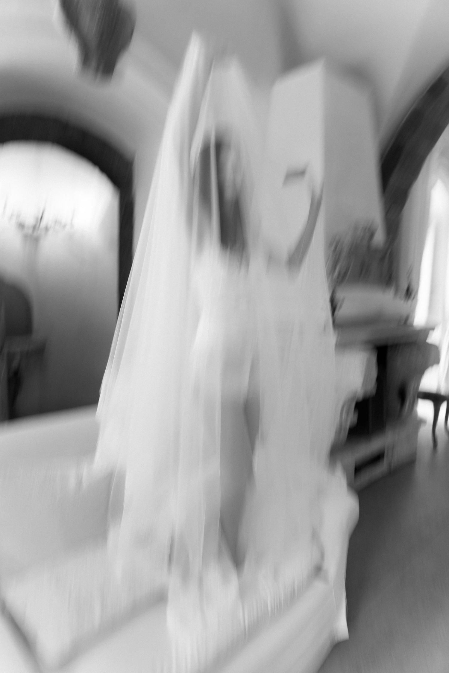 Blurry black and white photo of a bride in a wedding dress and veil inside an elegant venue.