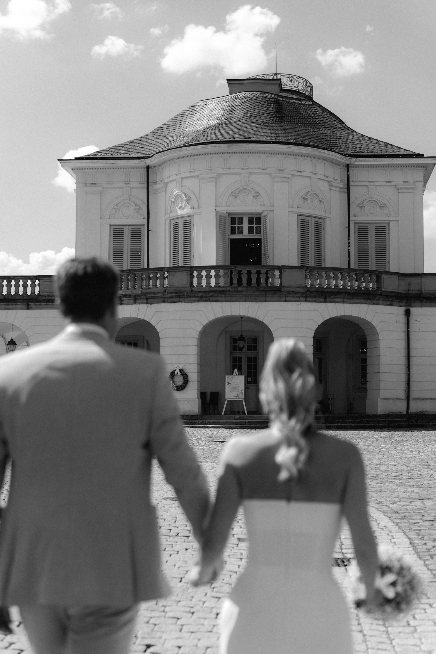 A black and white panoramic series of a wedding couple walking towards an elegant white mansion building. Schloss Solitude