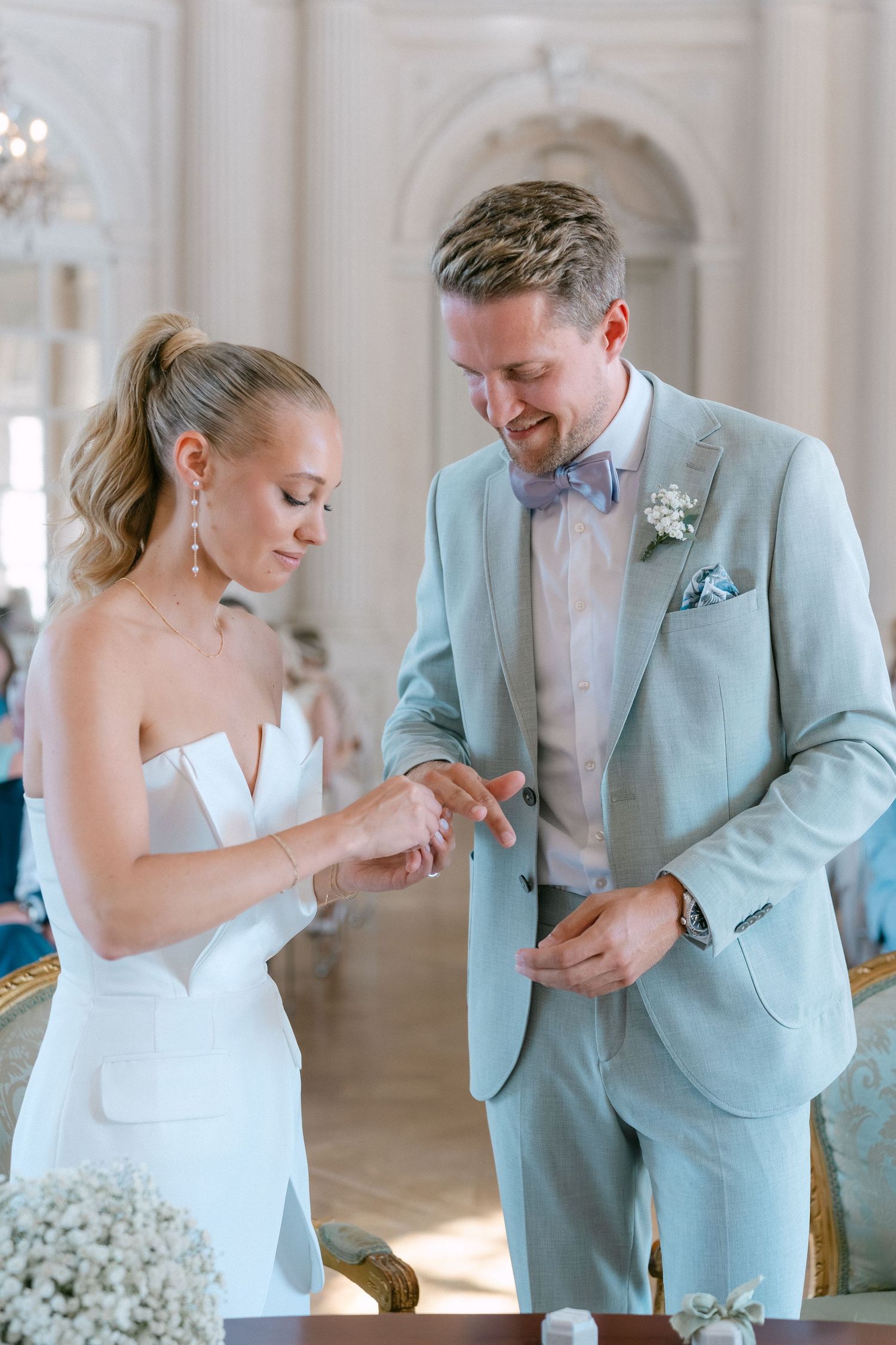 A couple shares a tender moment during their wedding ceremony as they exchange rings in an elegant light-filled venue. Schloss Solitude