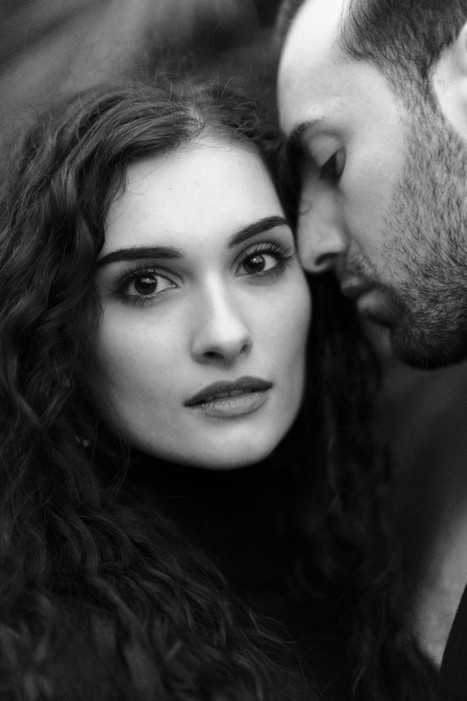 Black and white intimate portrait of a romantic couple in close proximity with dramatic lighting.