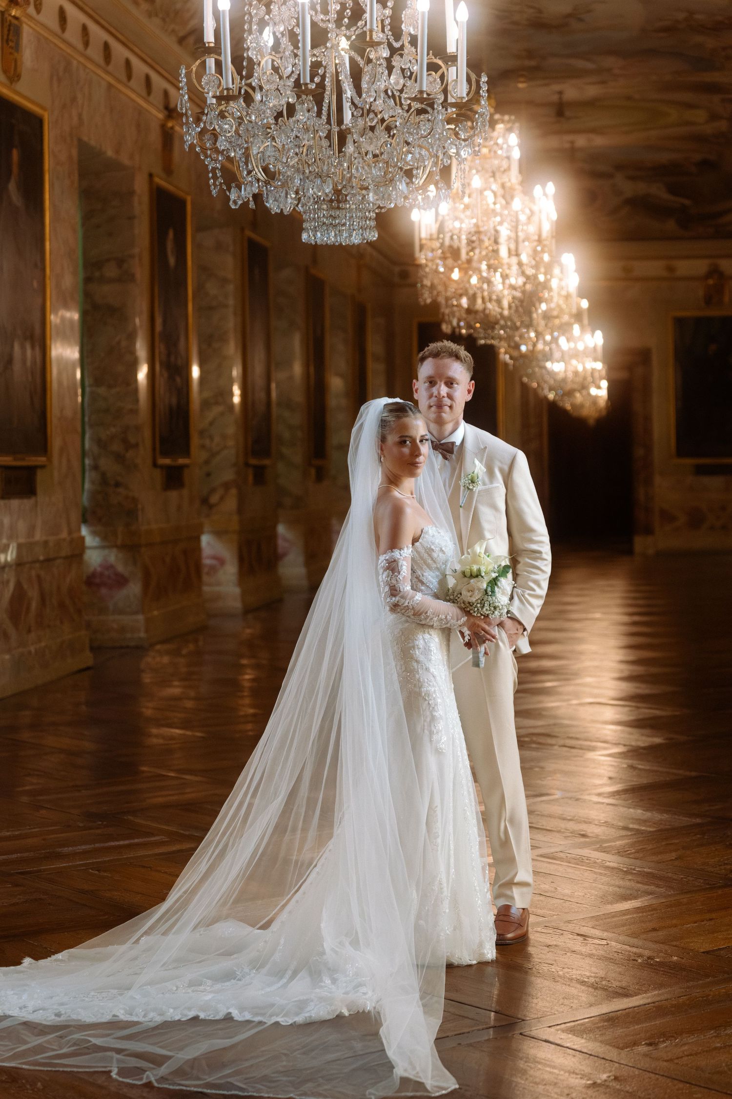 A romantic wedding couple embraces in an elegant ballroom with crystal chandeliers and polished wooden floors. Schloss Ludwigsburg