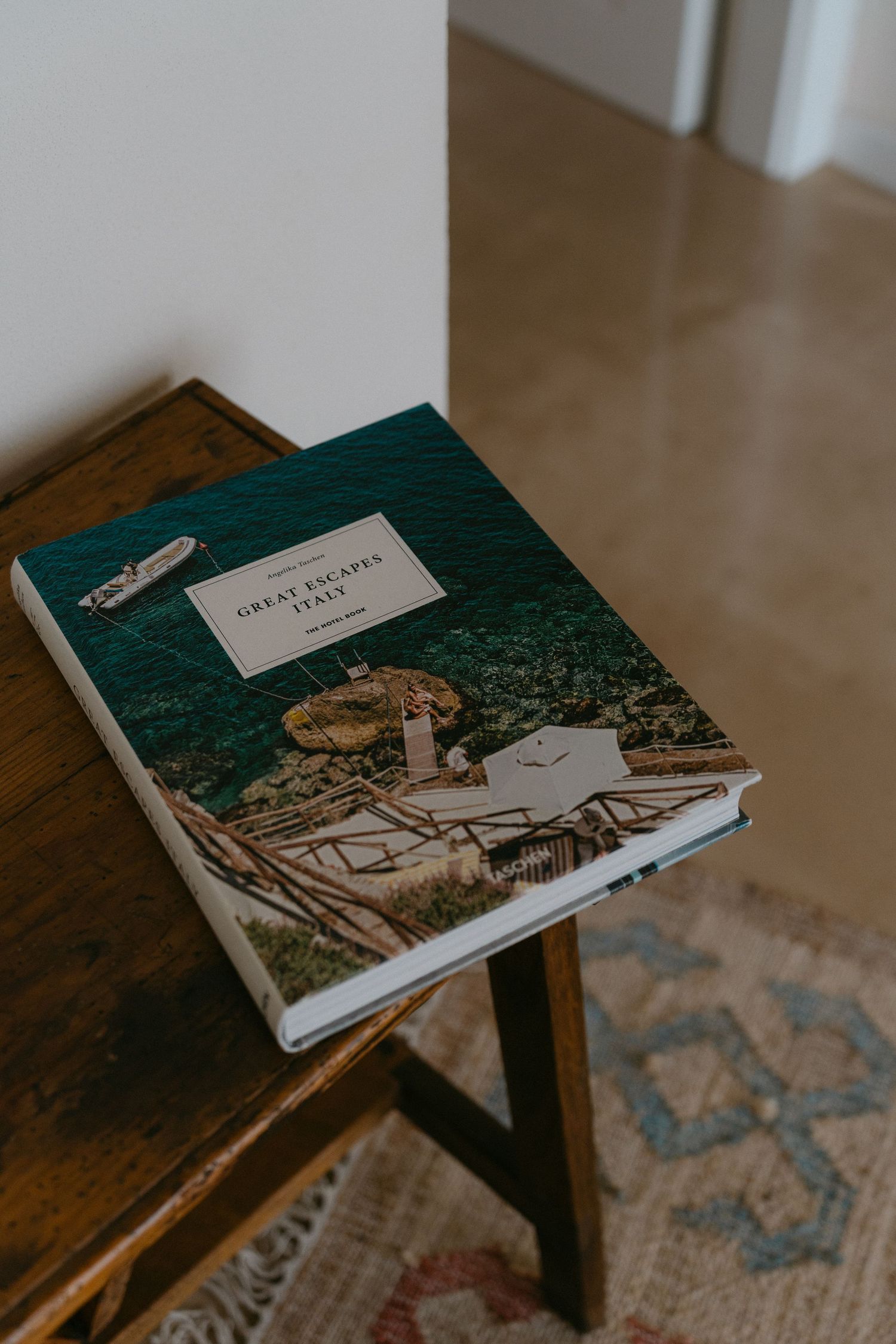 A green hardcover book resting on a wooden table with a decorative rug underneath.