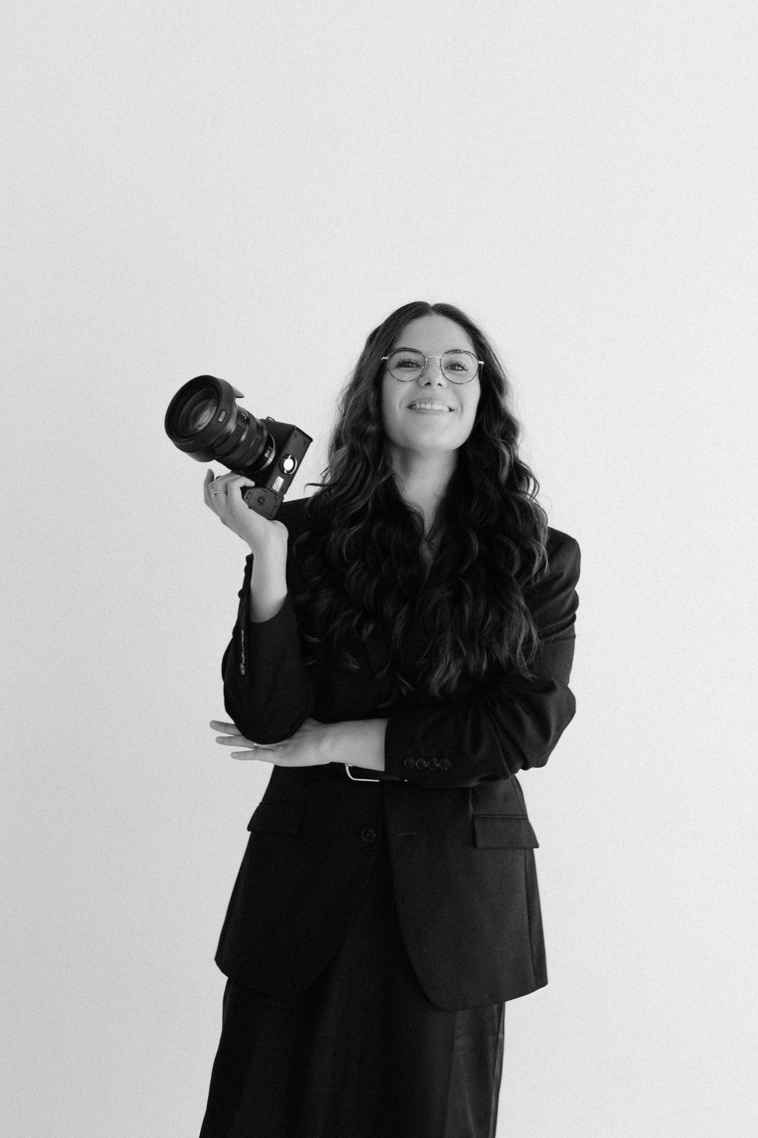 Black and white portrait of a smiling woman in a blazer holding a professional camera, ideal for photography services.