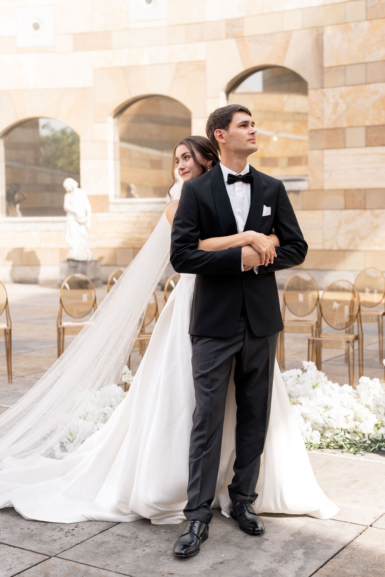 A bride and groom pose together on stone steps during their elegant outdoor wedding photoshoot.