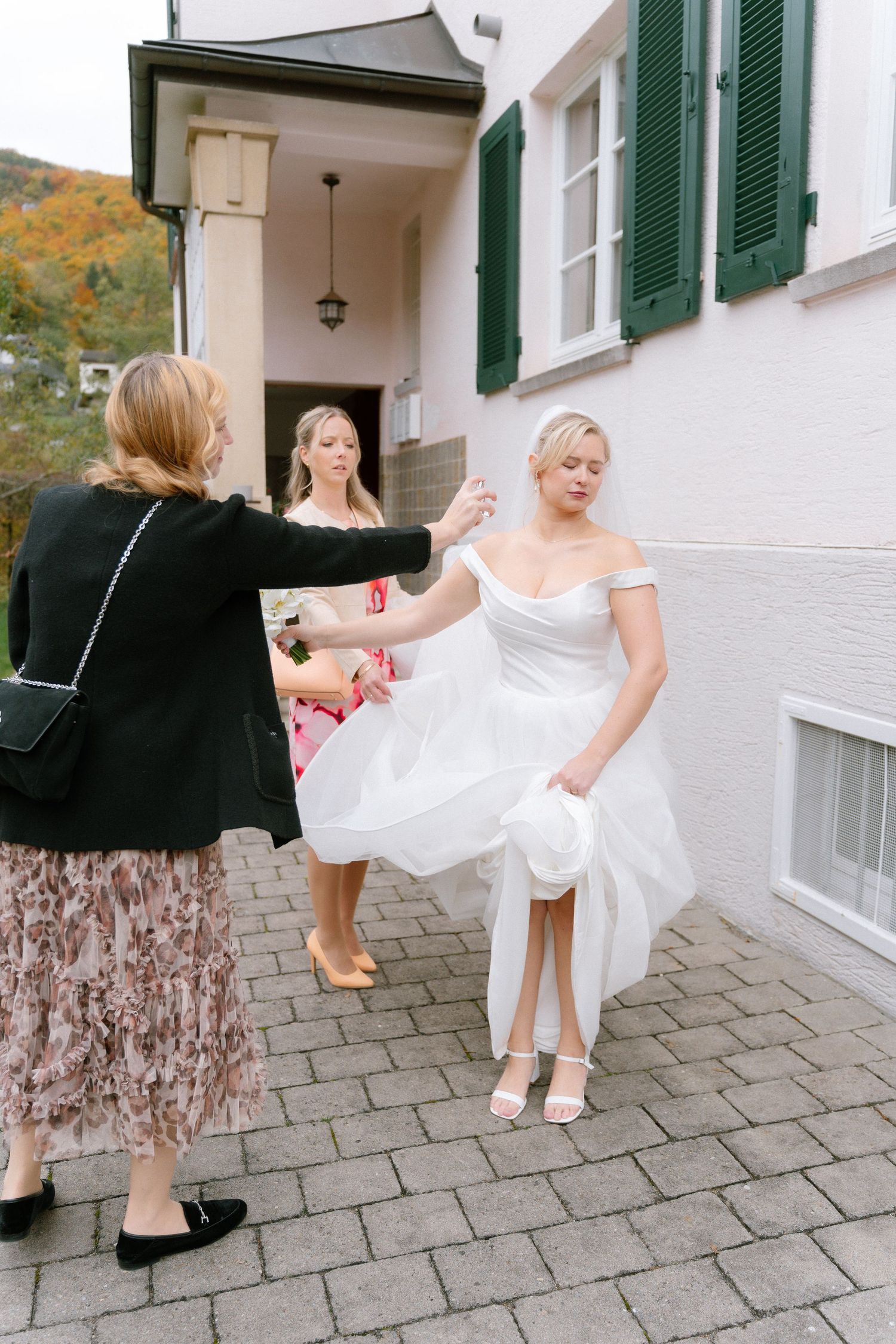 A series of four photos showing someone helping adjust a white wedding dress on stone pavement outside a building.