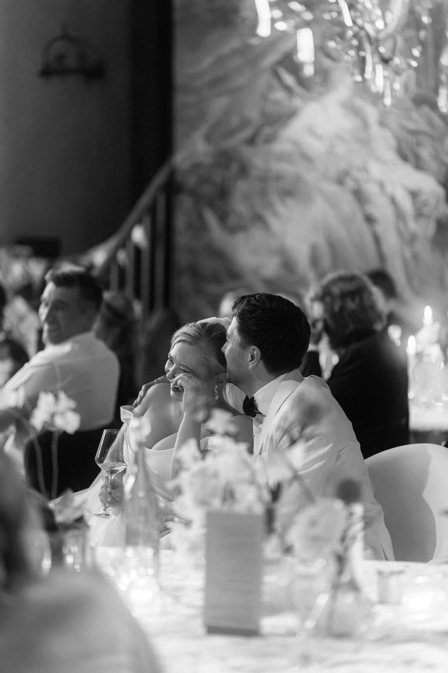 Black and white candid photo of wedding reception guests seated at elegant tables with candlelight and floral centerpieces.