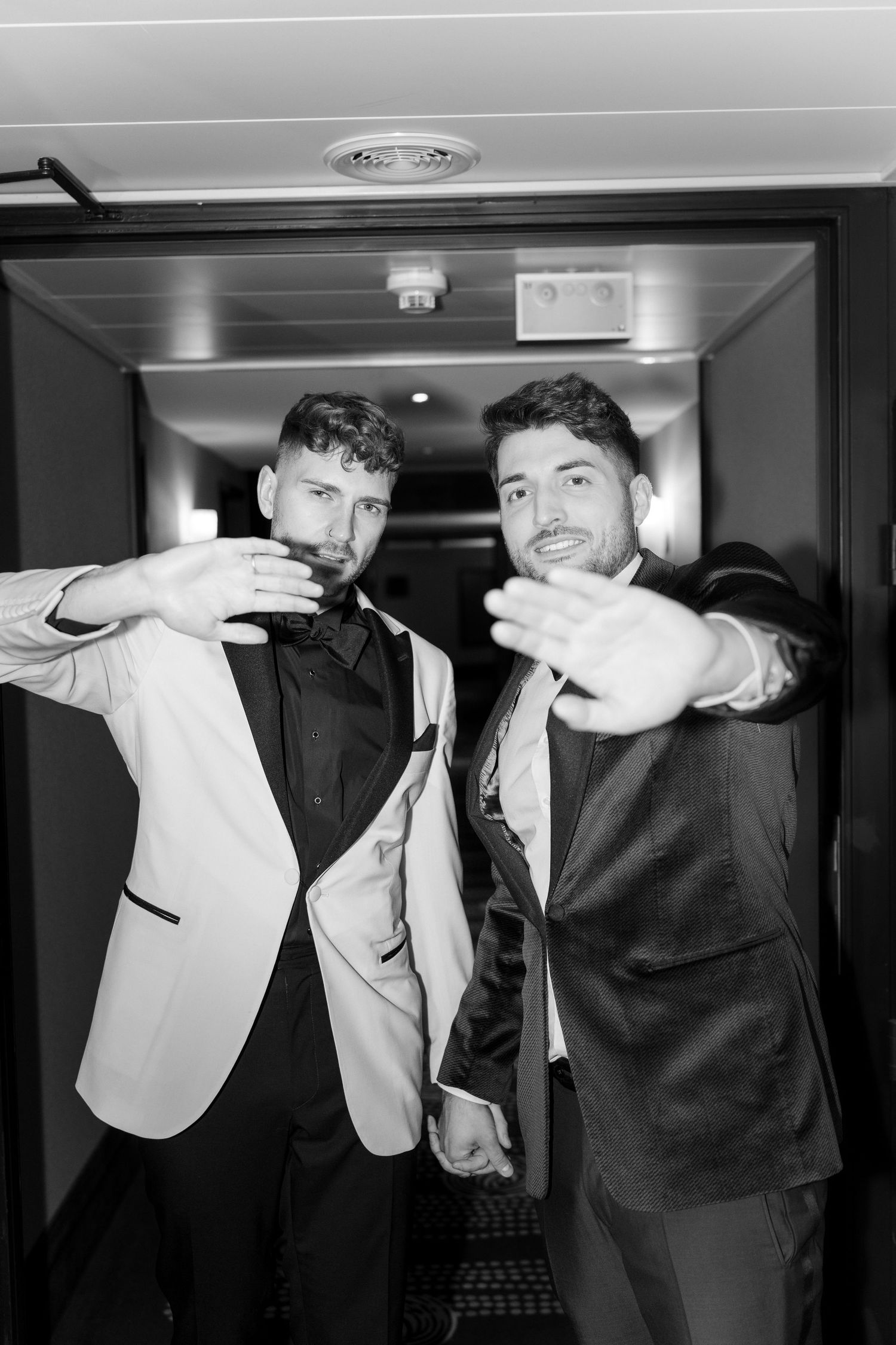 A black and white photo of two men in suits gesturing at the camera in what appears to be a hallway.