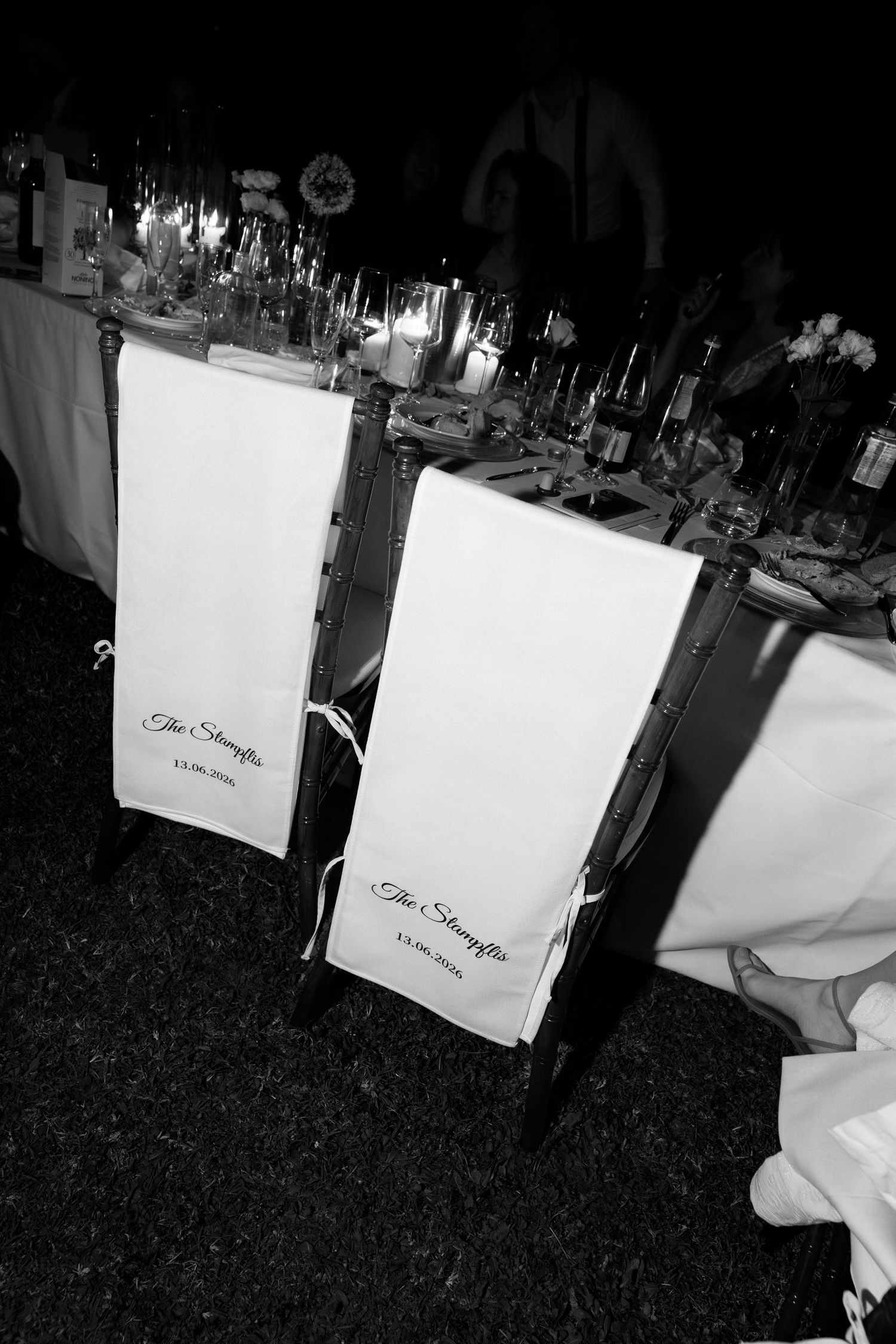Black and white photo of elegant wedding reception chairs with personalized white banners reading The Shaeffers at a candlelit table.