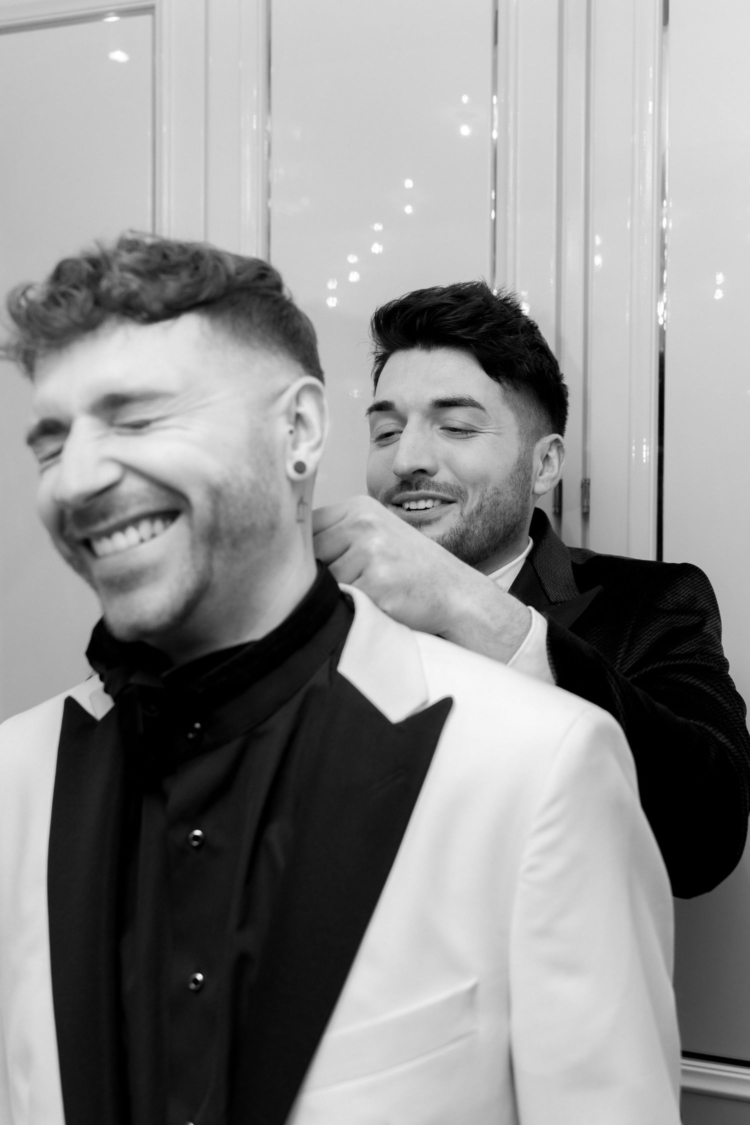 A candid black and white photo showing two men in formal attire sharing a joyful moment together.