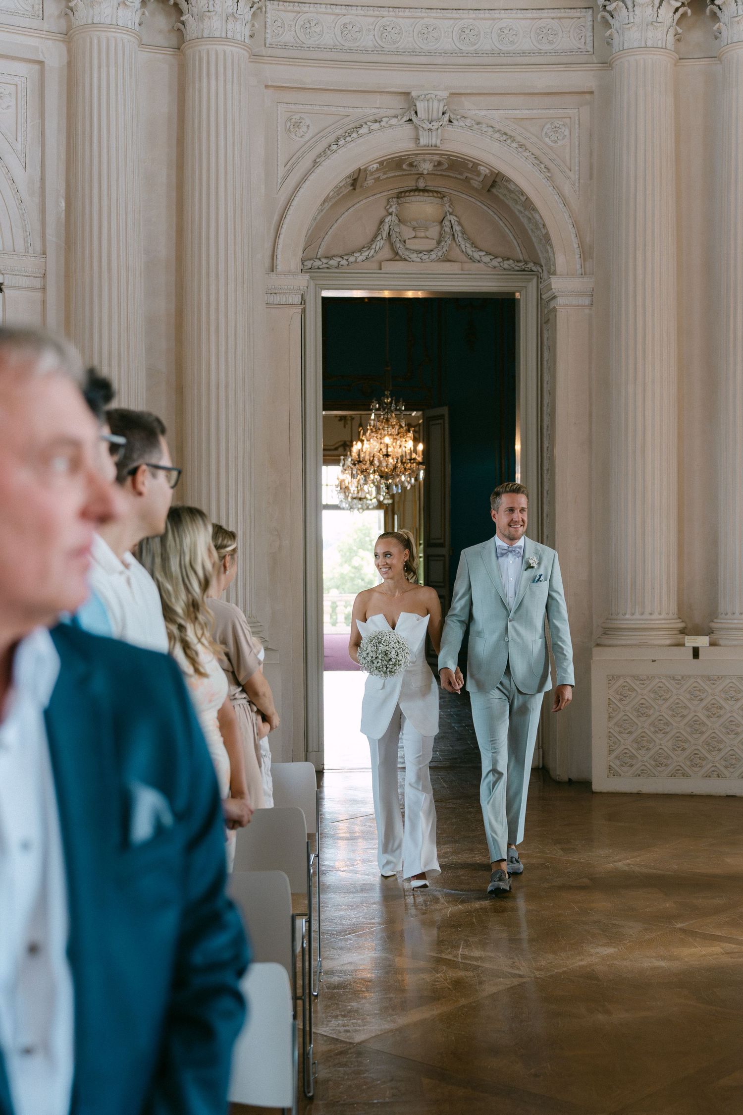 Elegant wedding ceremony in an ornate room with white columns, crystal chandelier and polished wooden floors. Schloss Solitude