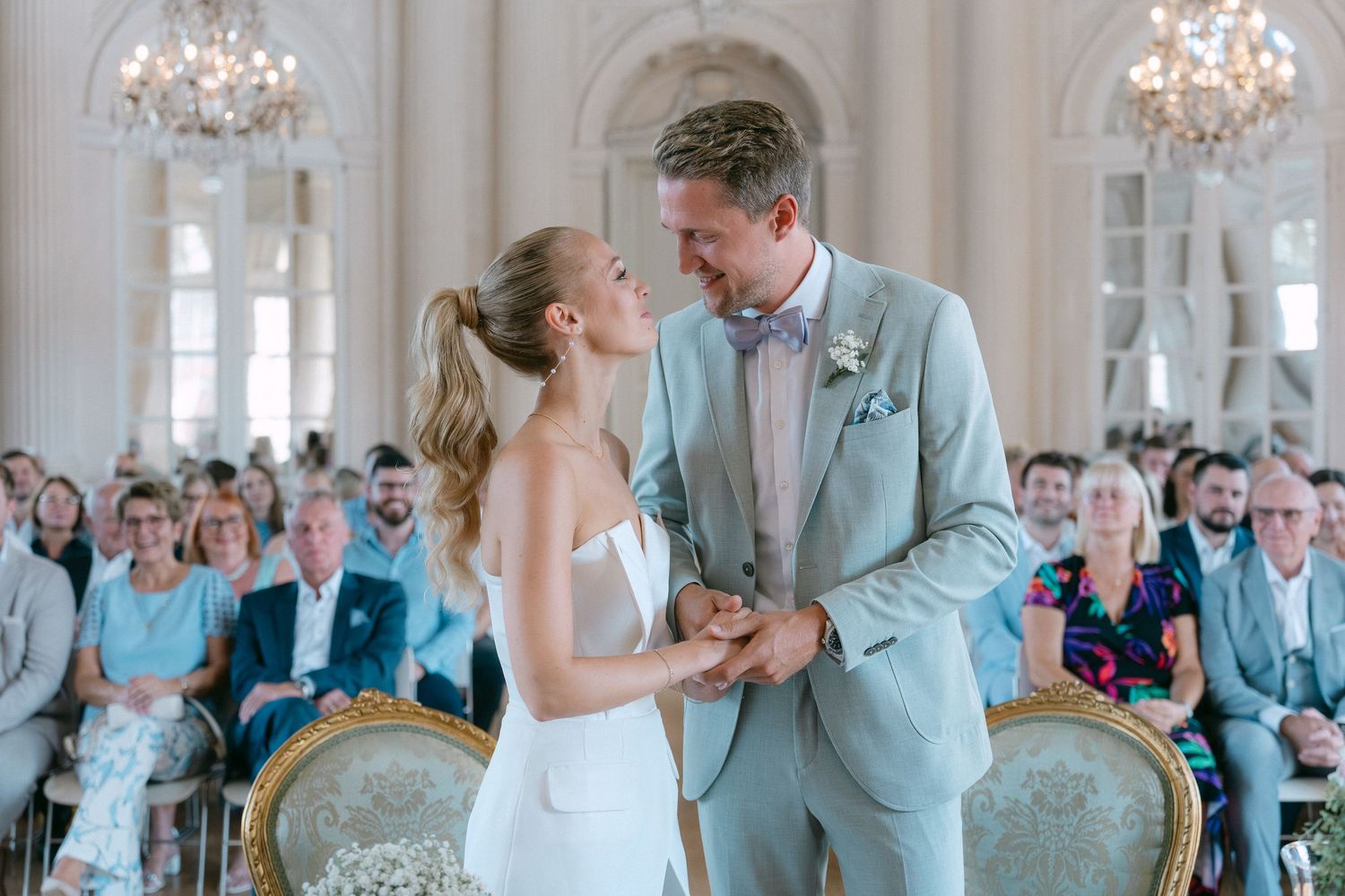 A couple shares their first dance at an elegant wedding ceremony in a grand ballroom with crystal chandeliers. Schloss Solitude