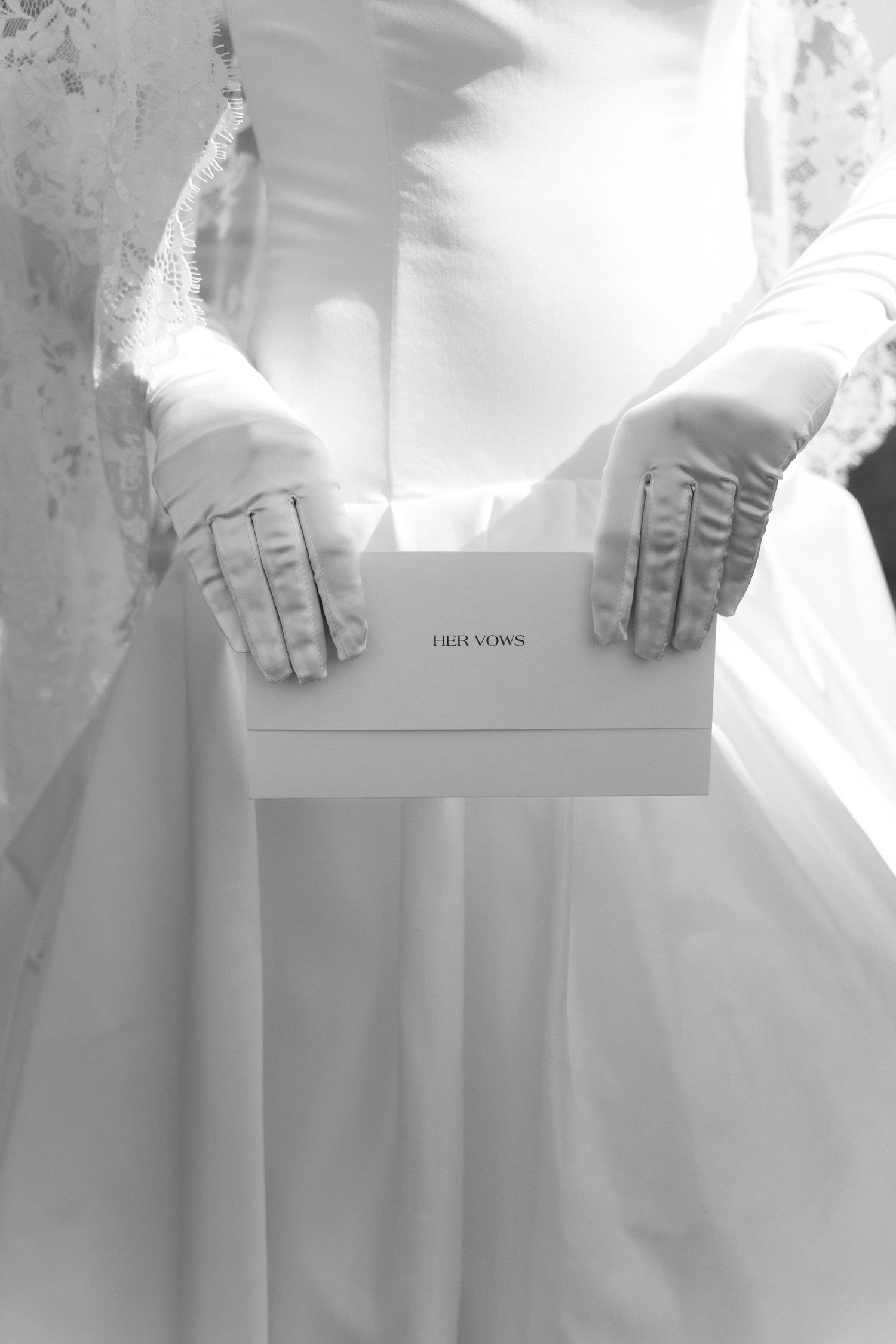 Bride in white gloves holding a Her Vows box in a black and white wedding photo.