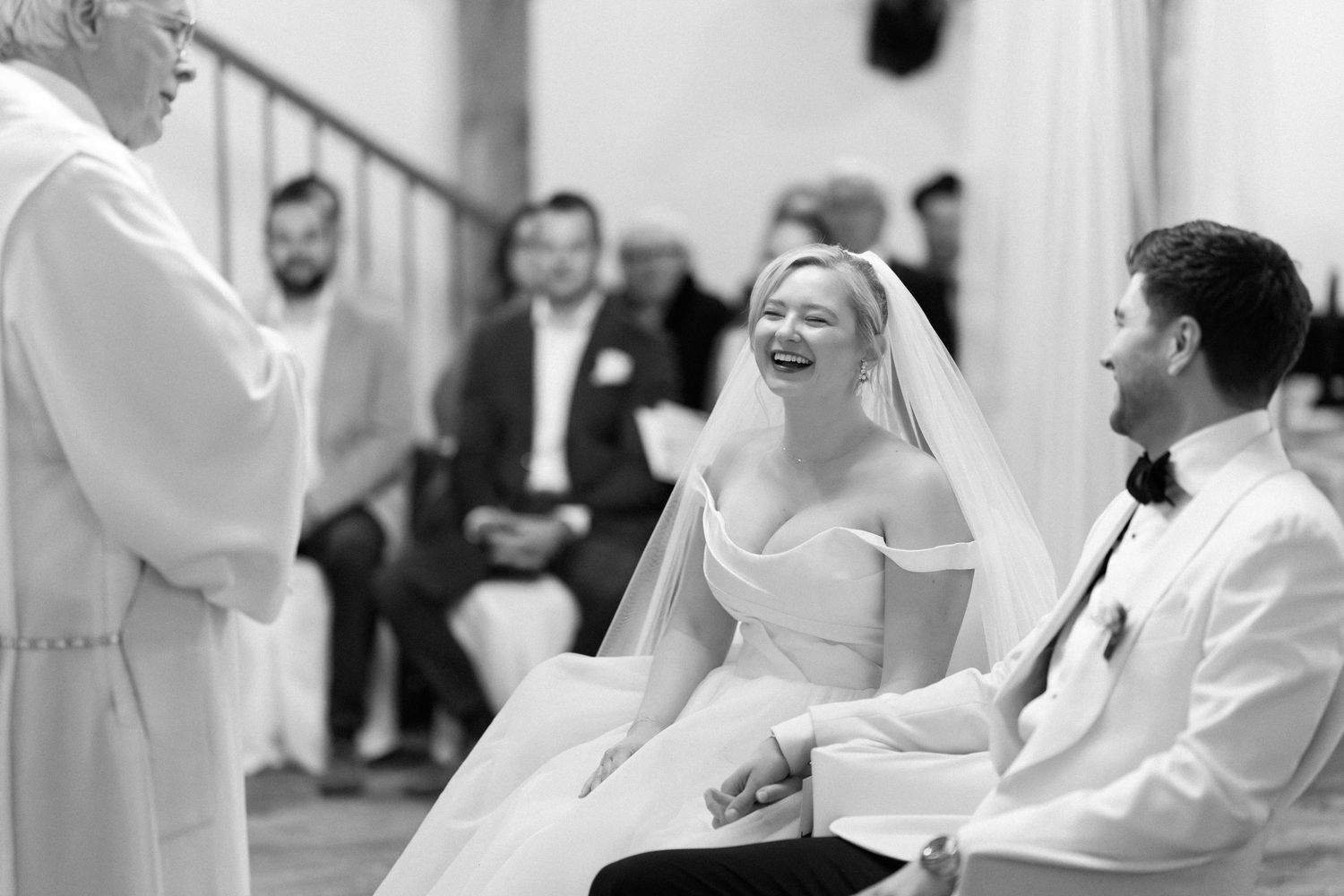 A joyful moment captured in black and white during a wedding ceremony as the couple shares a laugh with the officiant.