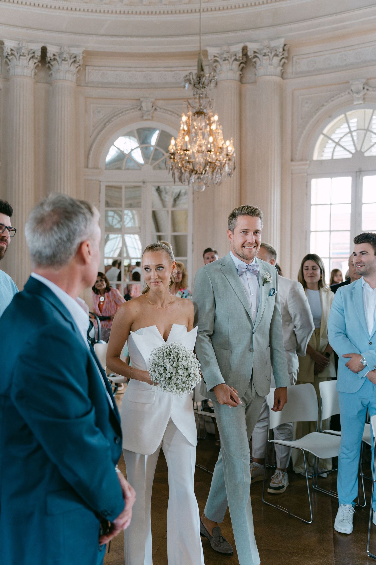 A wedding ceremony takes place in an elegant room with white columns and a crystal chandelier. Schloss Solitude