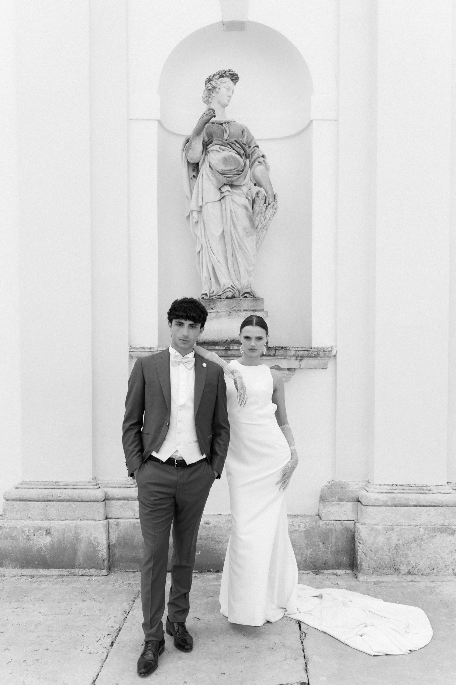 Black and white wedding photos showing couple posing against white wall with classical statues in background. Villa Mosconi Bertani