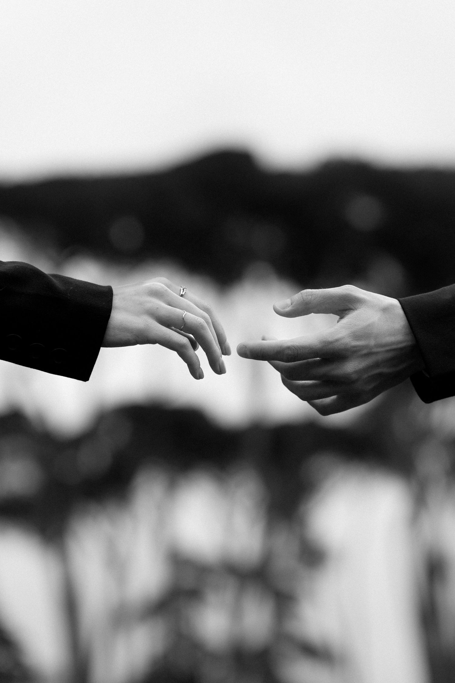 Two hands reach out toward each other against a blurred background in a black and white artistic photograph.