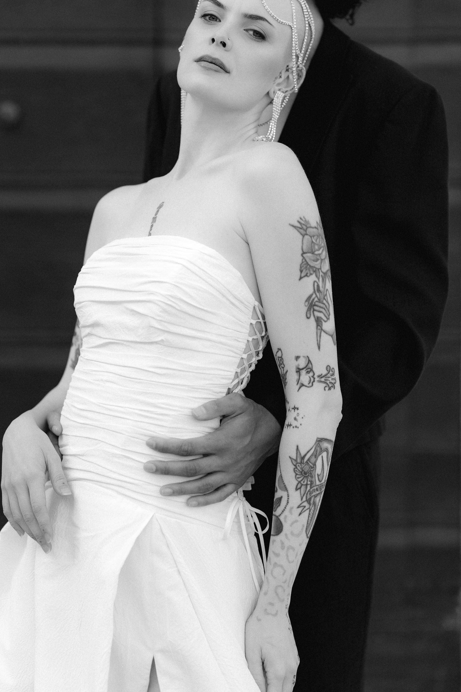 A series of black and white photos showing someone in a white strapless dress with visible arm tattoos striking elegant poses.