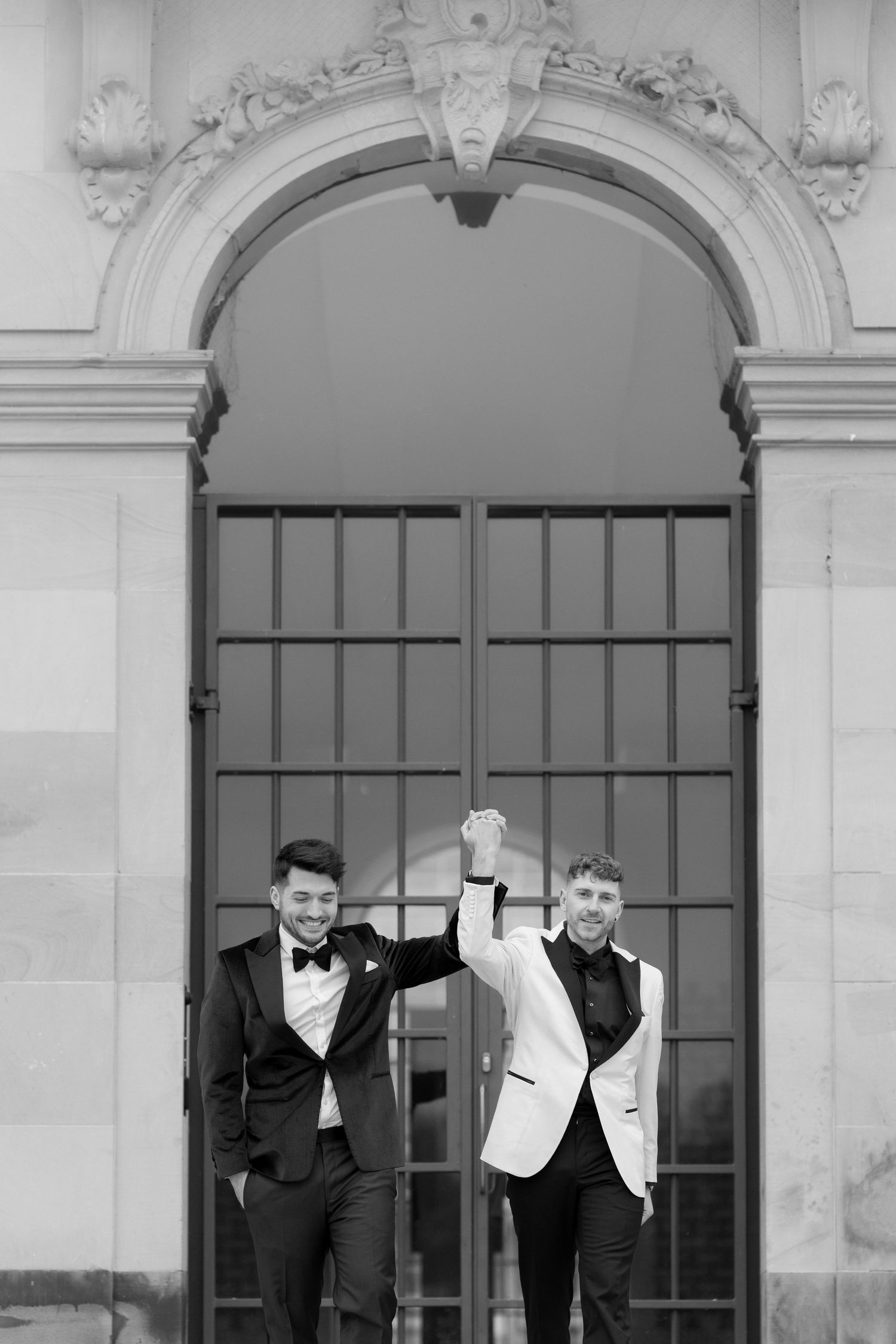 Two people in formal attire stand beneath an ornate archway with decorative molding in a black and white photo.
