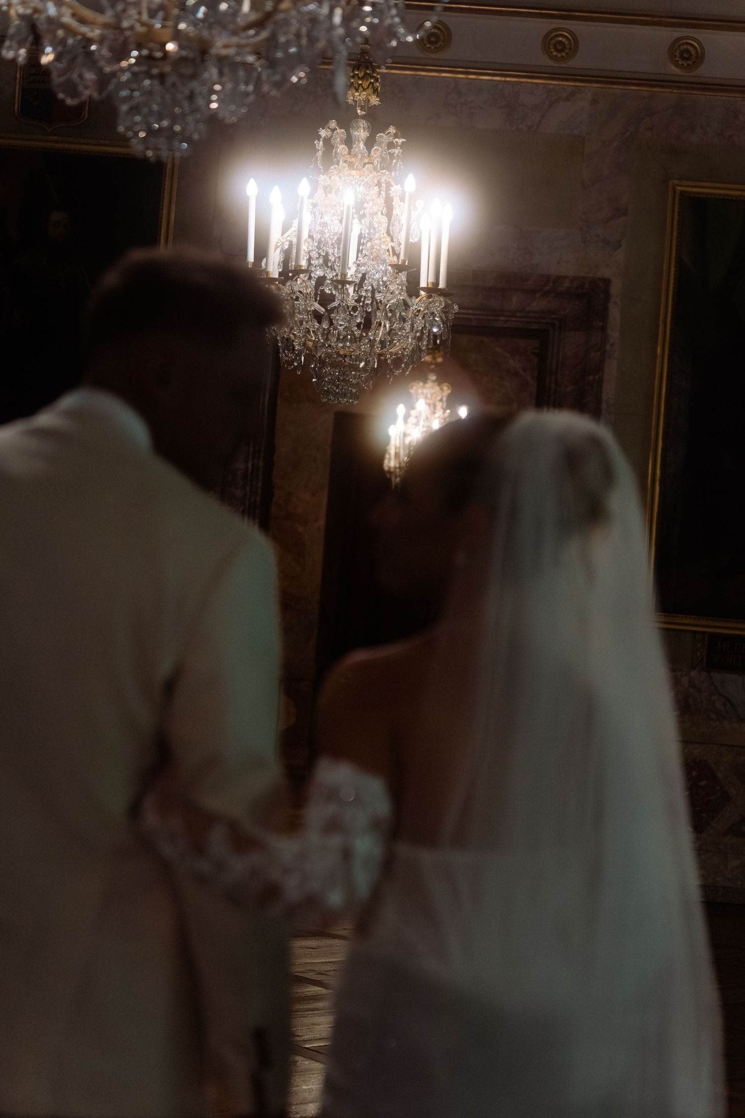 A couple shares a romantic dance under an elegant crystal chandelier in a dimly lit ballroom. Schloss Ludwigsburg