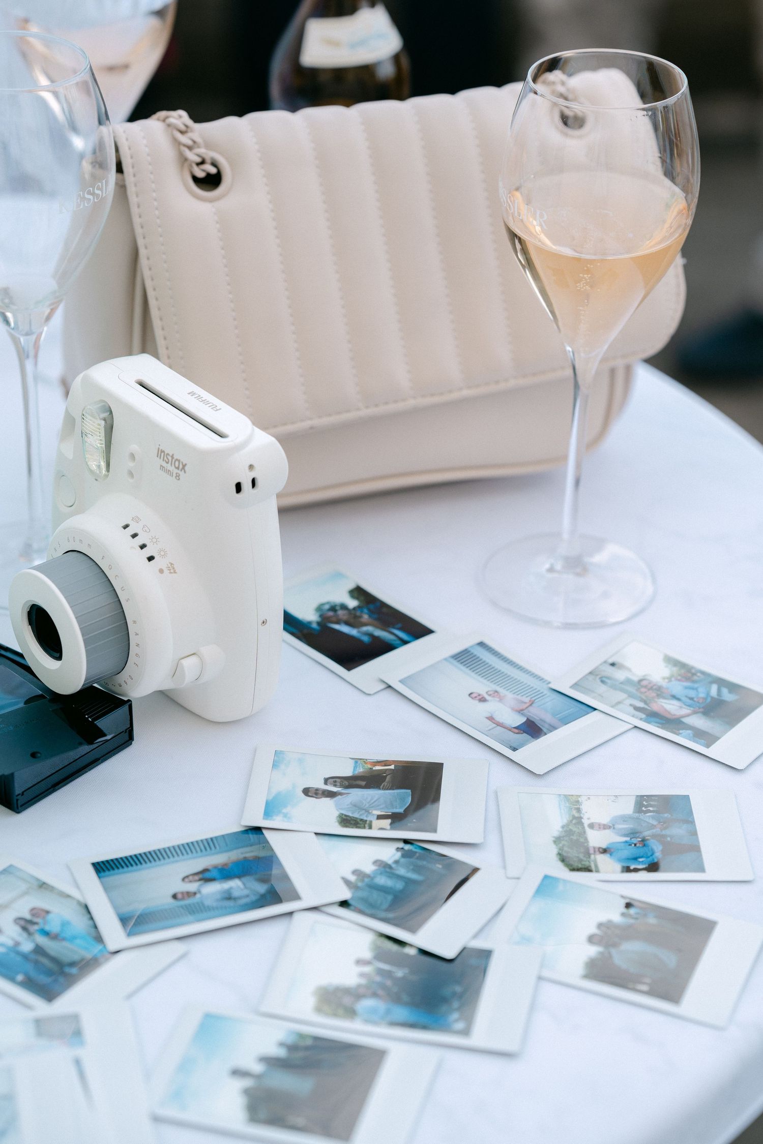 Polaroid photos and a white retro camera displayed on a white table with a wine glass and soft lighting. Schloss Solitude