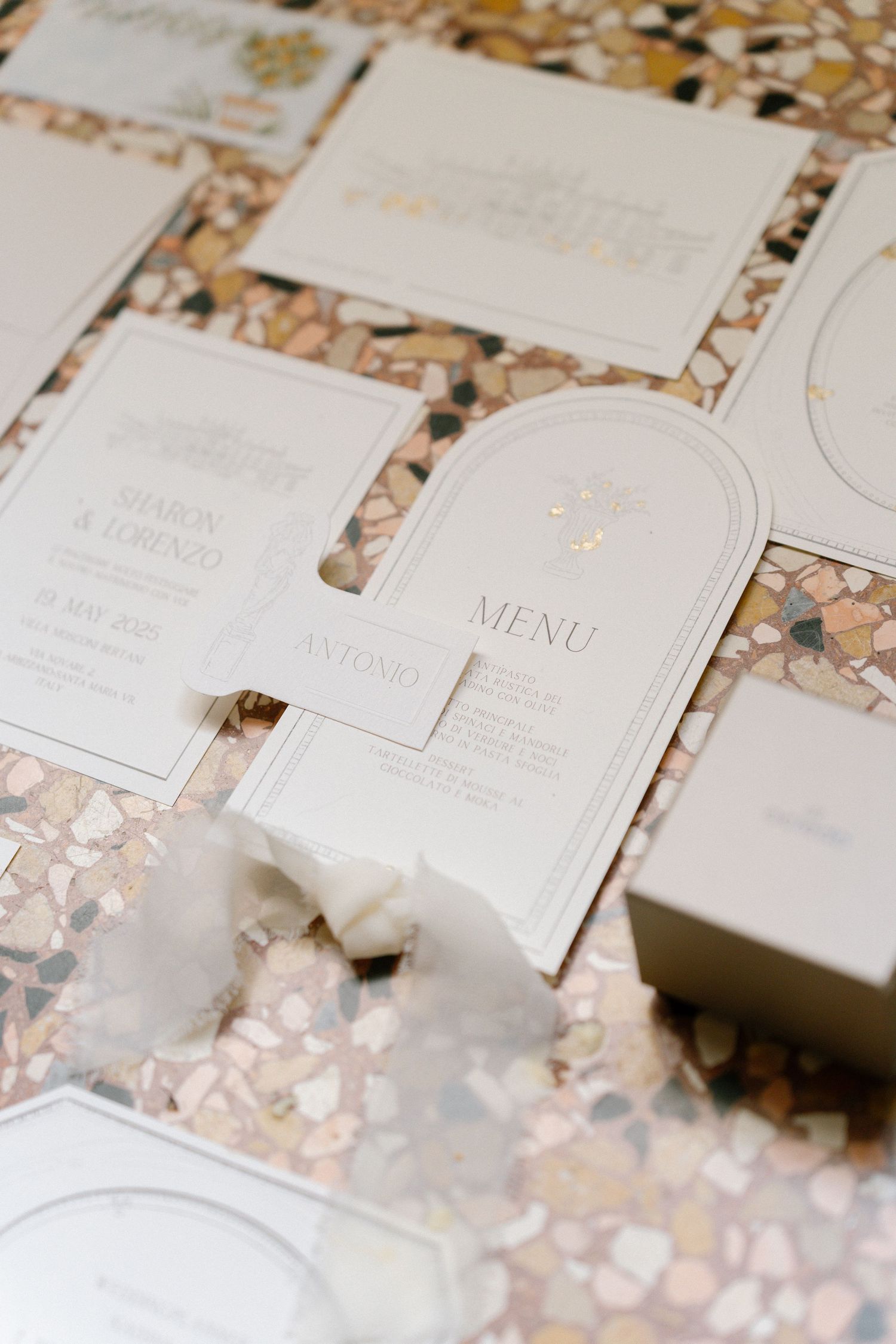 Elegant white wedding menu cards and stationery displayed on a shimmering rose gold sequined surface. Villa Mosconi Bertani