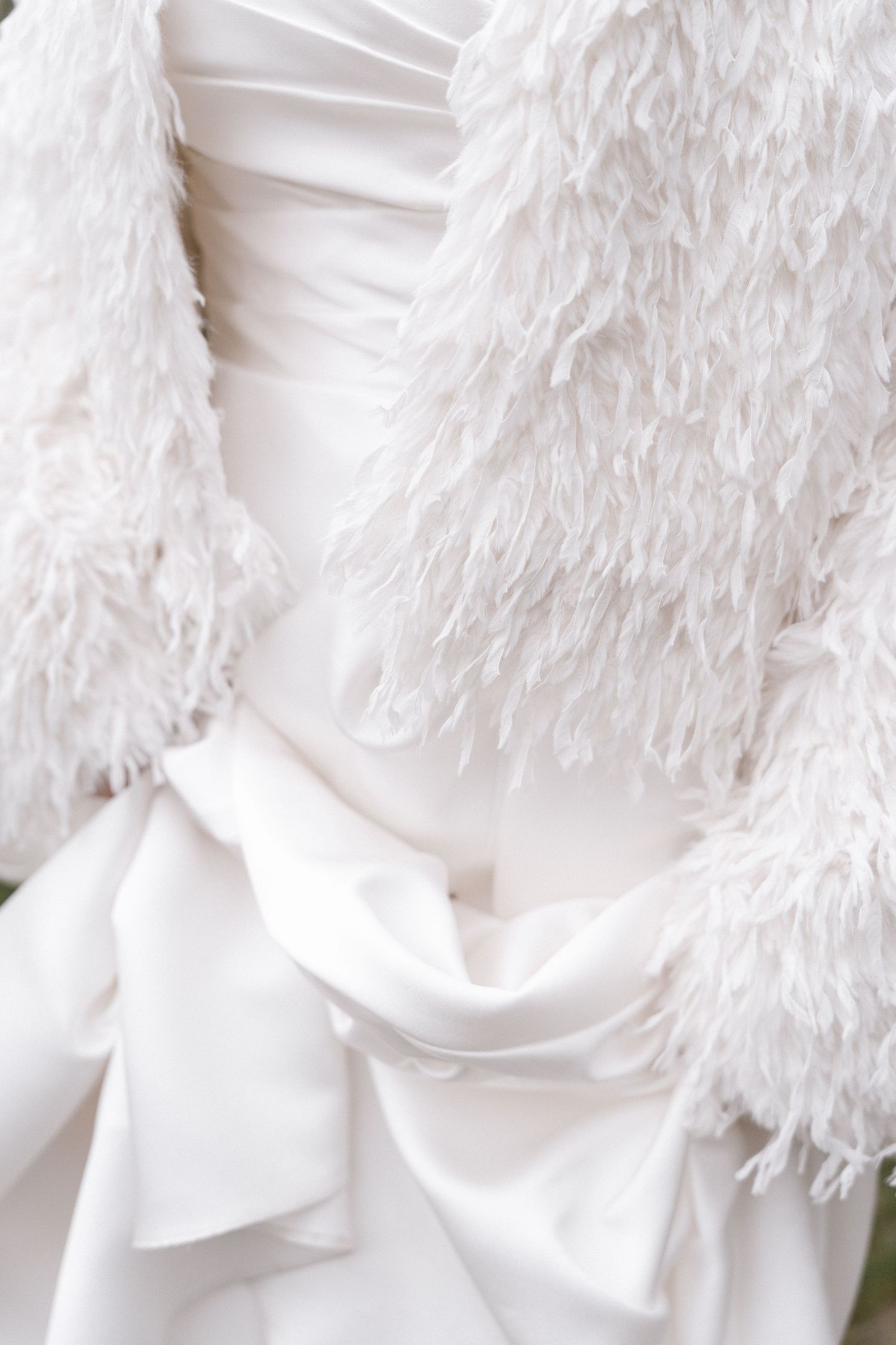 Close-up of an elegant white wedding dress featuring a satin bow, ruched bodice, and fluffy feather trim jacket.