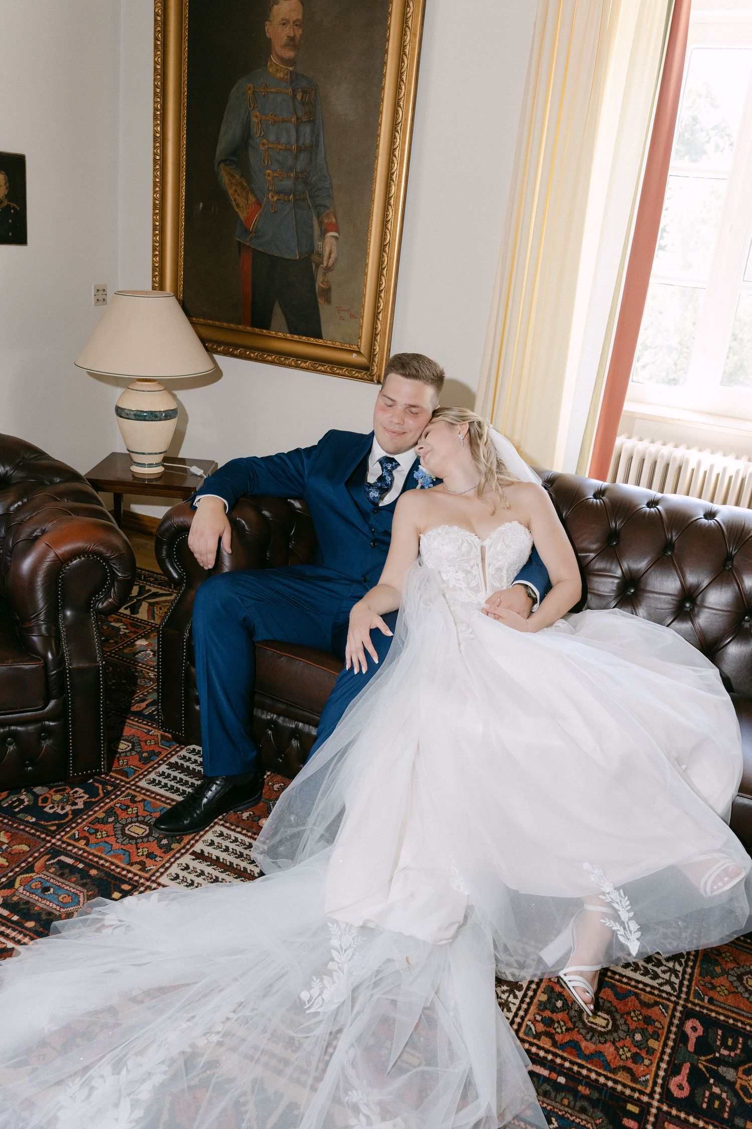 Couple relaxes on vintage leather couch with bride's flowing white dress spread across furniture.