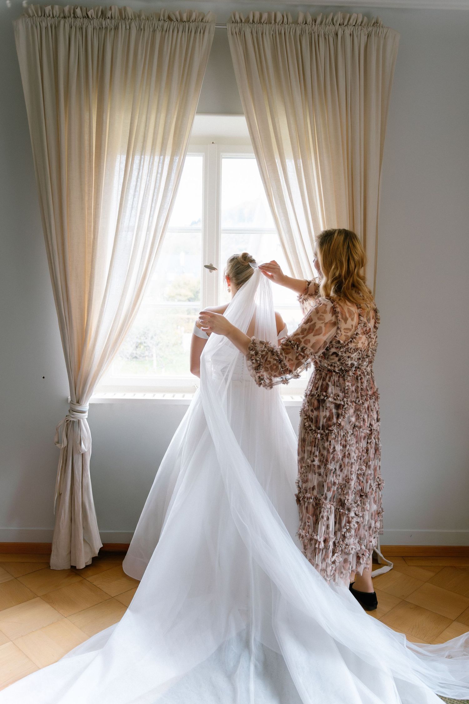 A woman in a floral dress adjusts white curtains by a bright window in a sequence of elegant movements.