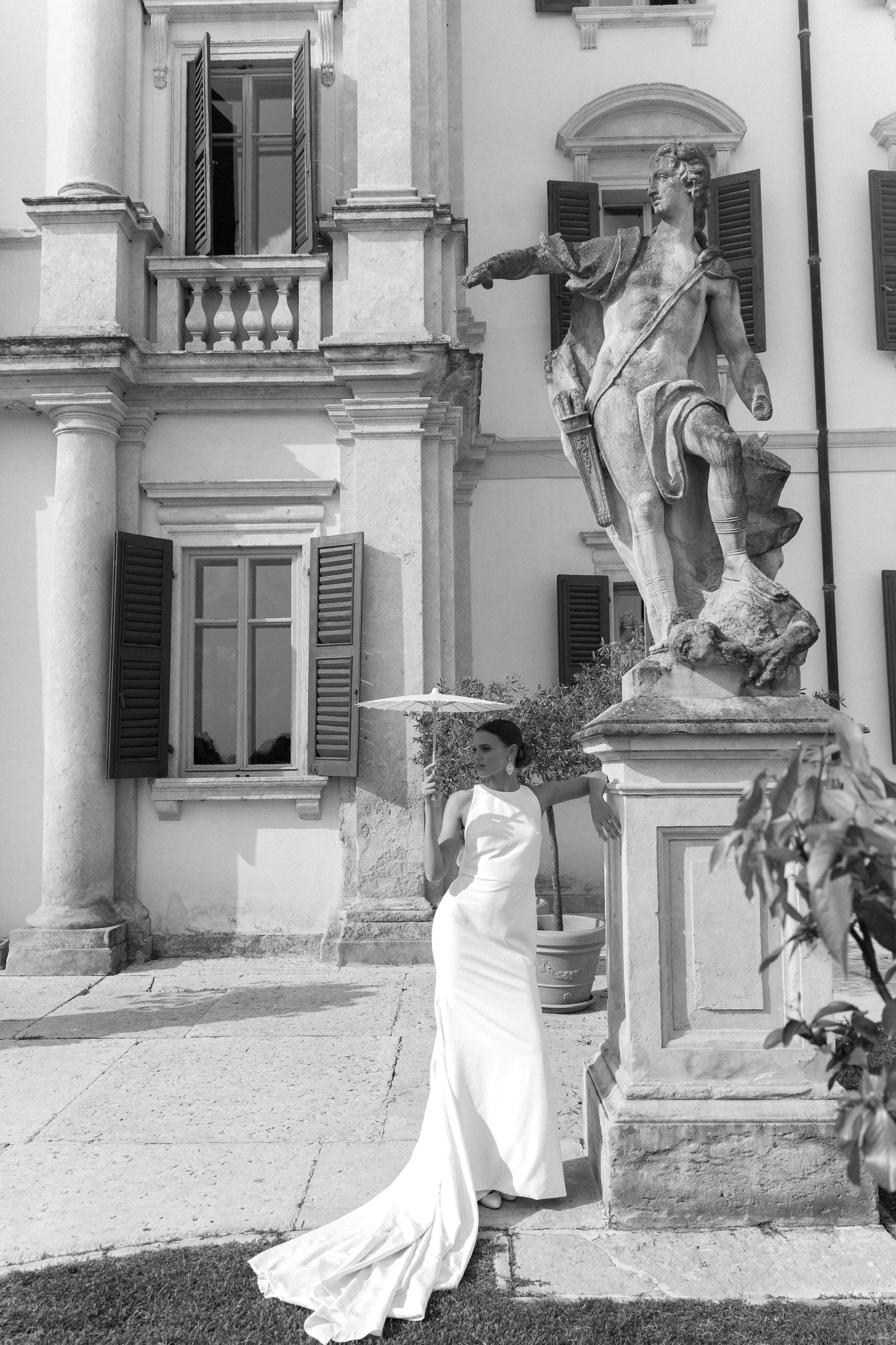 A sequence of four black and white photos showing a person in a flowing white dress posing in front of a classical building. Villa Mosconi B
