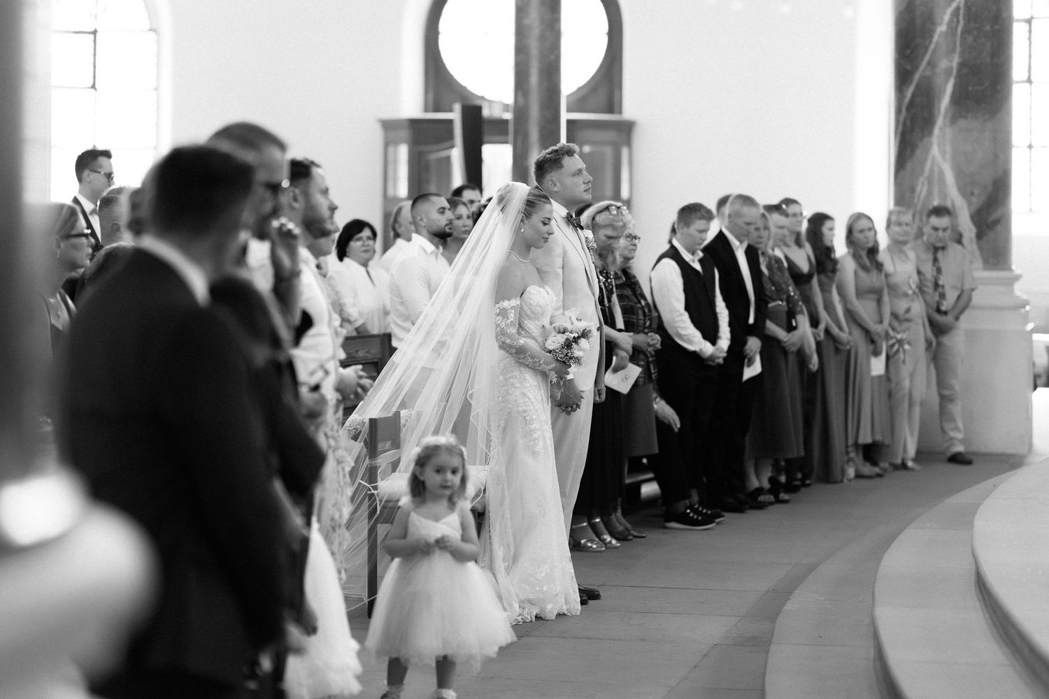 A black and white photograph of a wedding ceremony with a bride in a veil and flower girl at a church entrance.