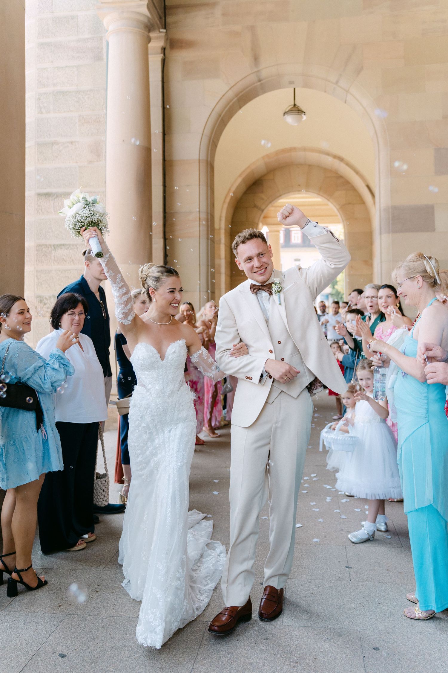 Wedding party celebrates with a playful champagne toast under elegant stone archways.