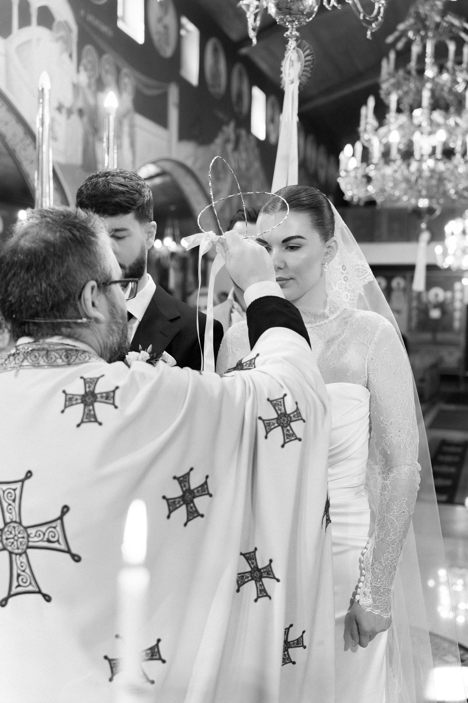 Orthodox priest placing wedding crowns on bride and groom during traditional church ceremony in black and white.