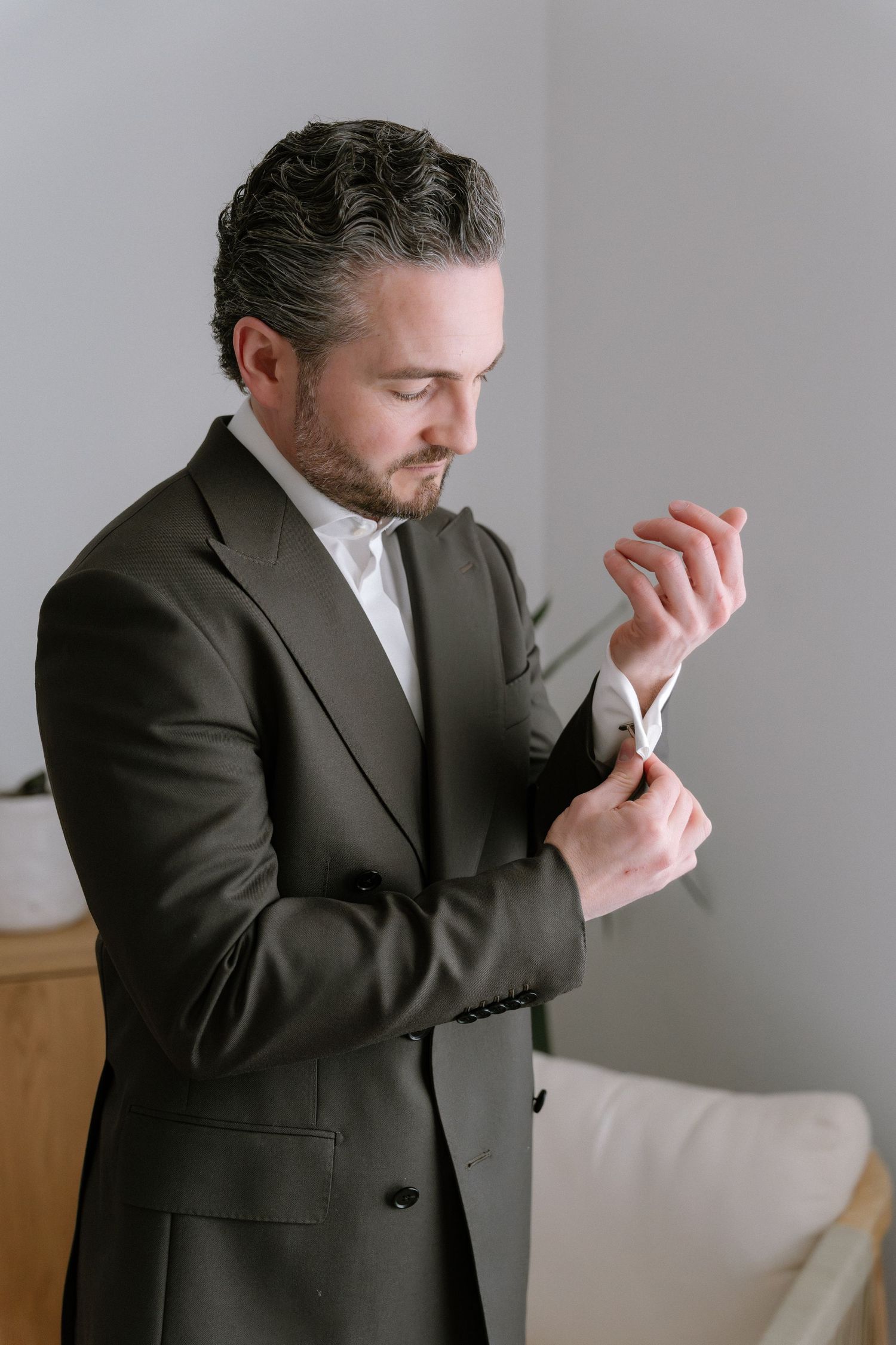 A well-dressed man in a dark suit adjusts his cufflinks while getting ready for a formal event.