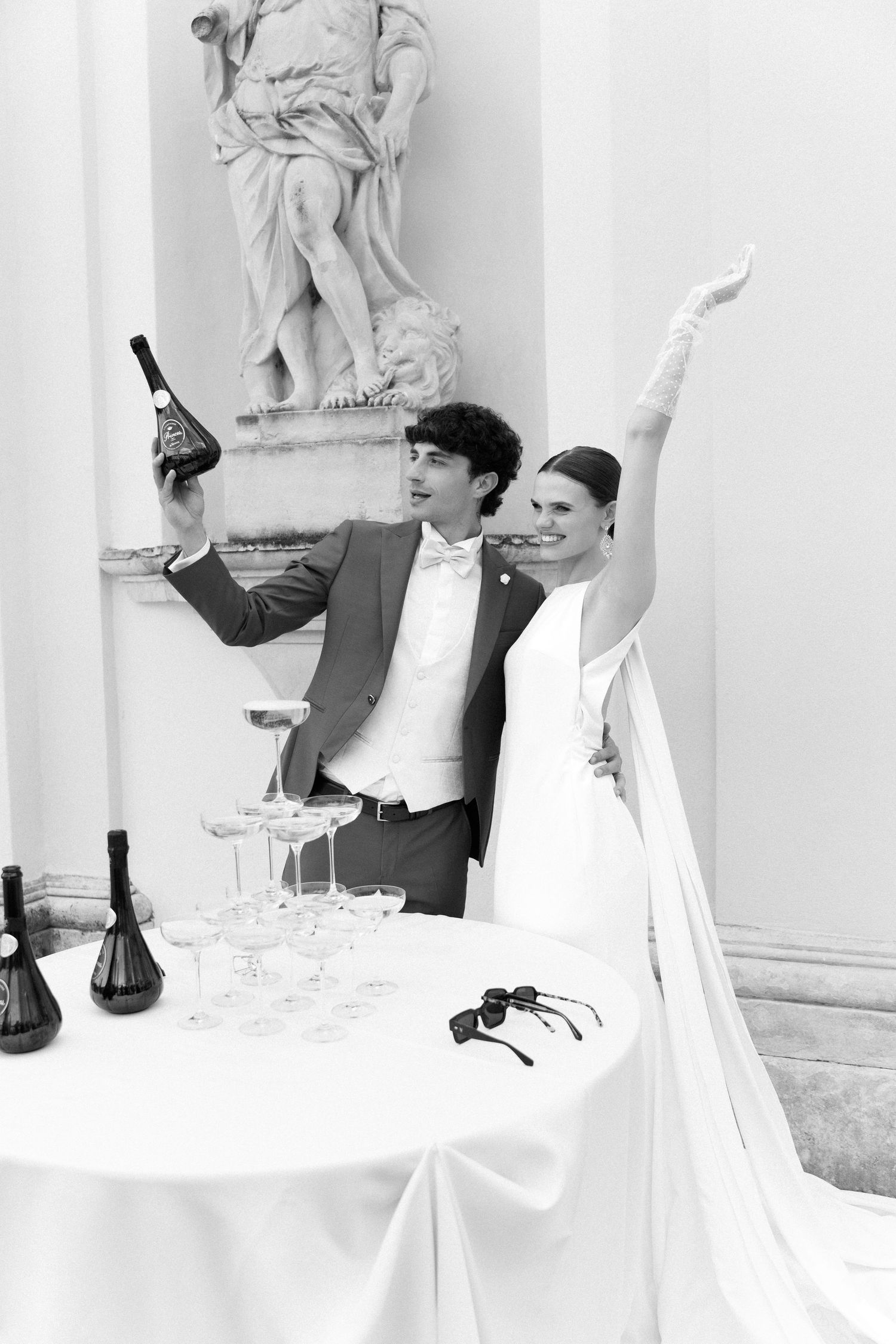 Black and white photo of bride and groom celebrating with champagne bottle at elegant wedding reception.