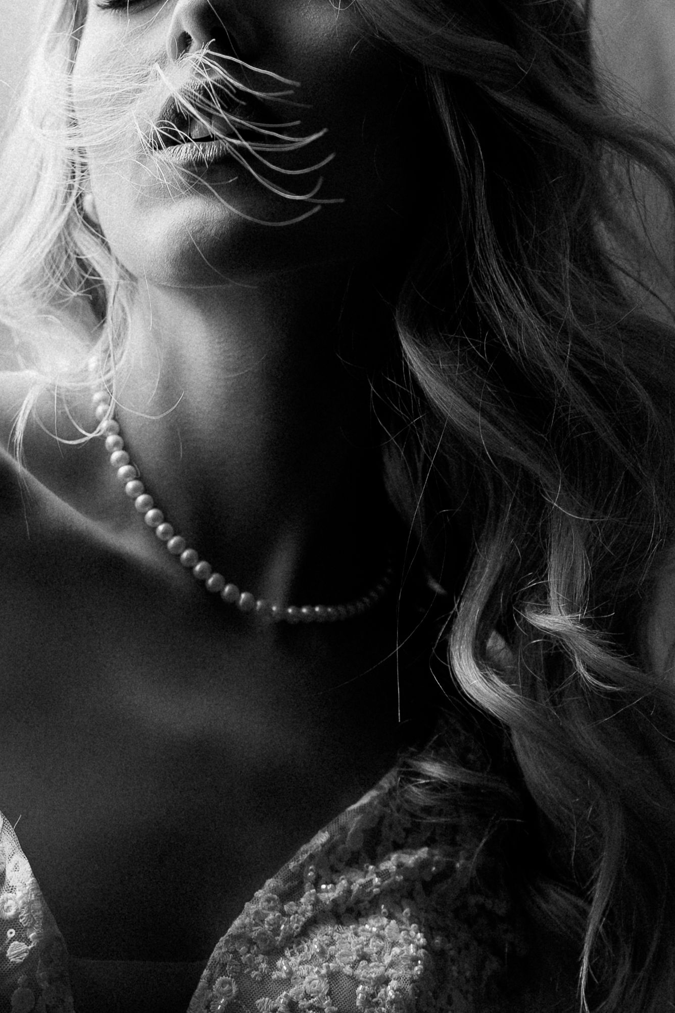A black and white portrait photograph shows a side profile with curled hair and a beaded necklace in dramatic lighting.